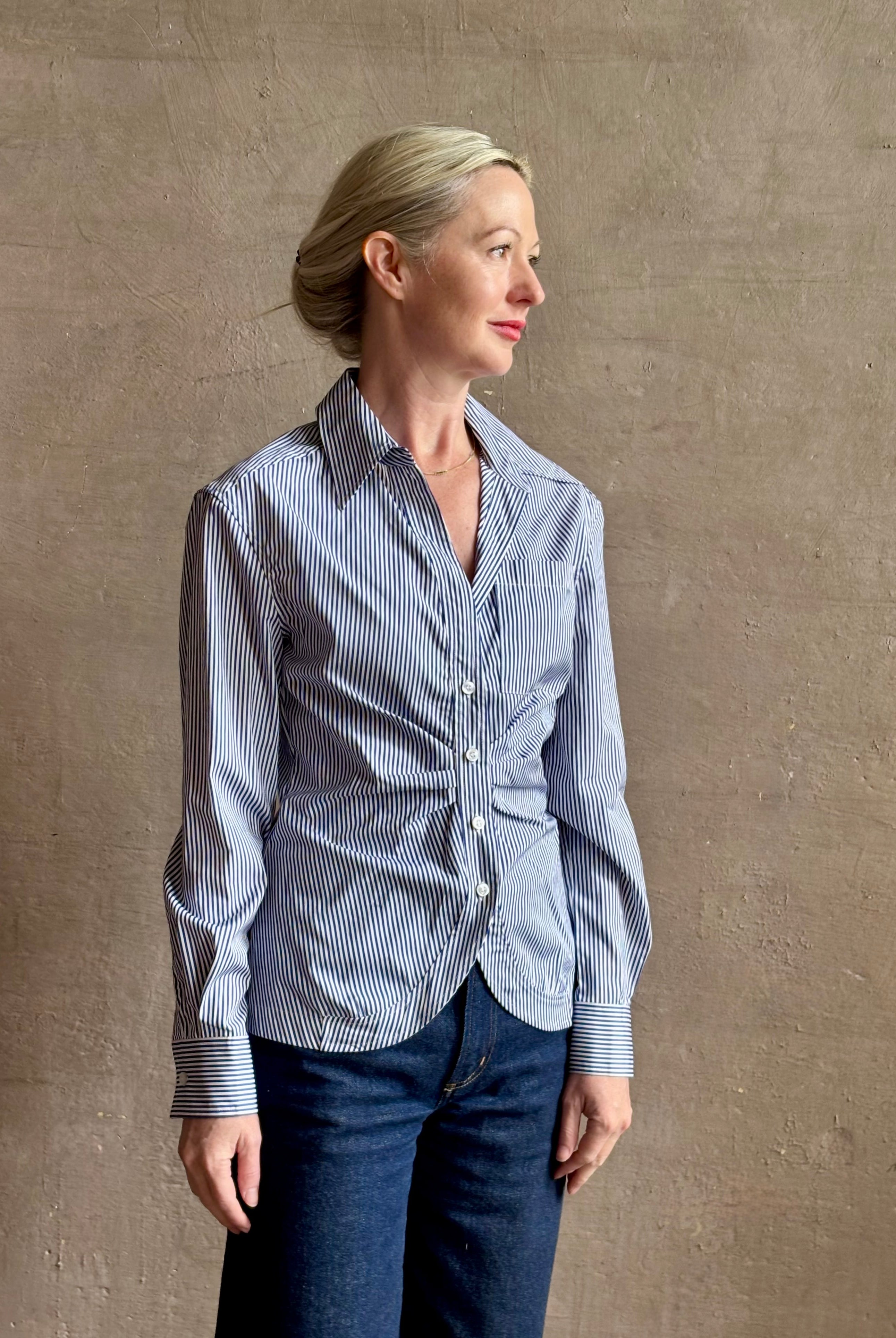 Mature woman wearing the European tailored Sierra Shirt from Callas rendered in a crisp navy and white stripe and crafted from cotton poplin featuring a flattering ruched front , long sleeves, v-neck and rounded bottom detail