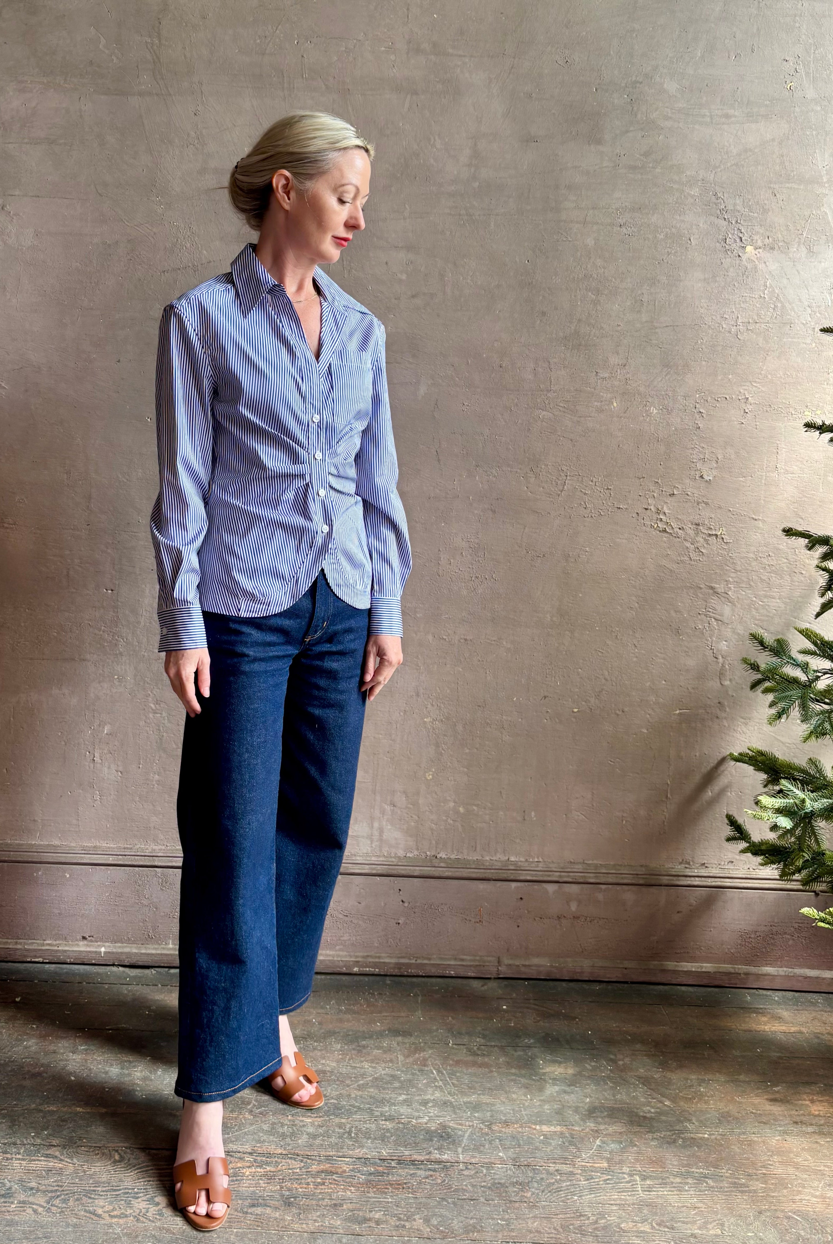 Mature woman wearing the European tailored Sierra Shirt from Callas rendered in a crisp navy and white stripe and crafted from cotton poplin featuring a flattering ruched front , long sleeves, v-neck and rounded bottom detail