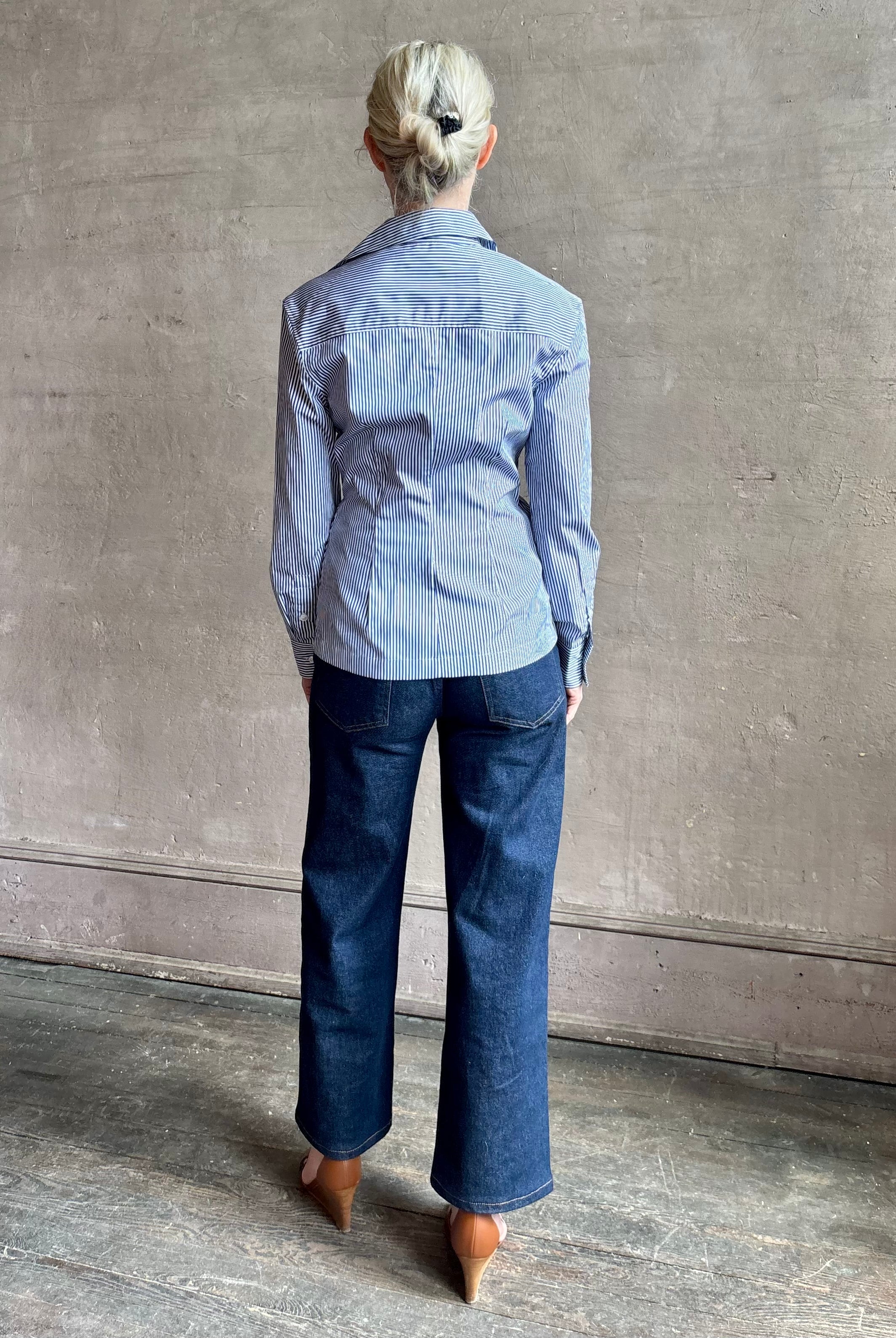 Mature woman wearing the European tailored Sierra Shirt from Callas rendered in a crisp navy and white stripe and crafted from cotton poplin featuring a flattering ruched front , long sleeves, v-neck and rounded bottom detail