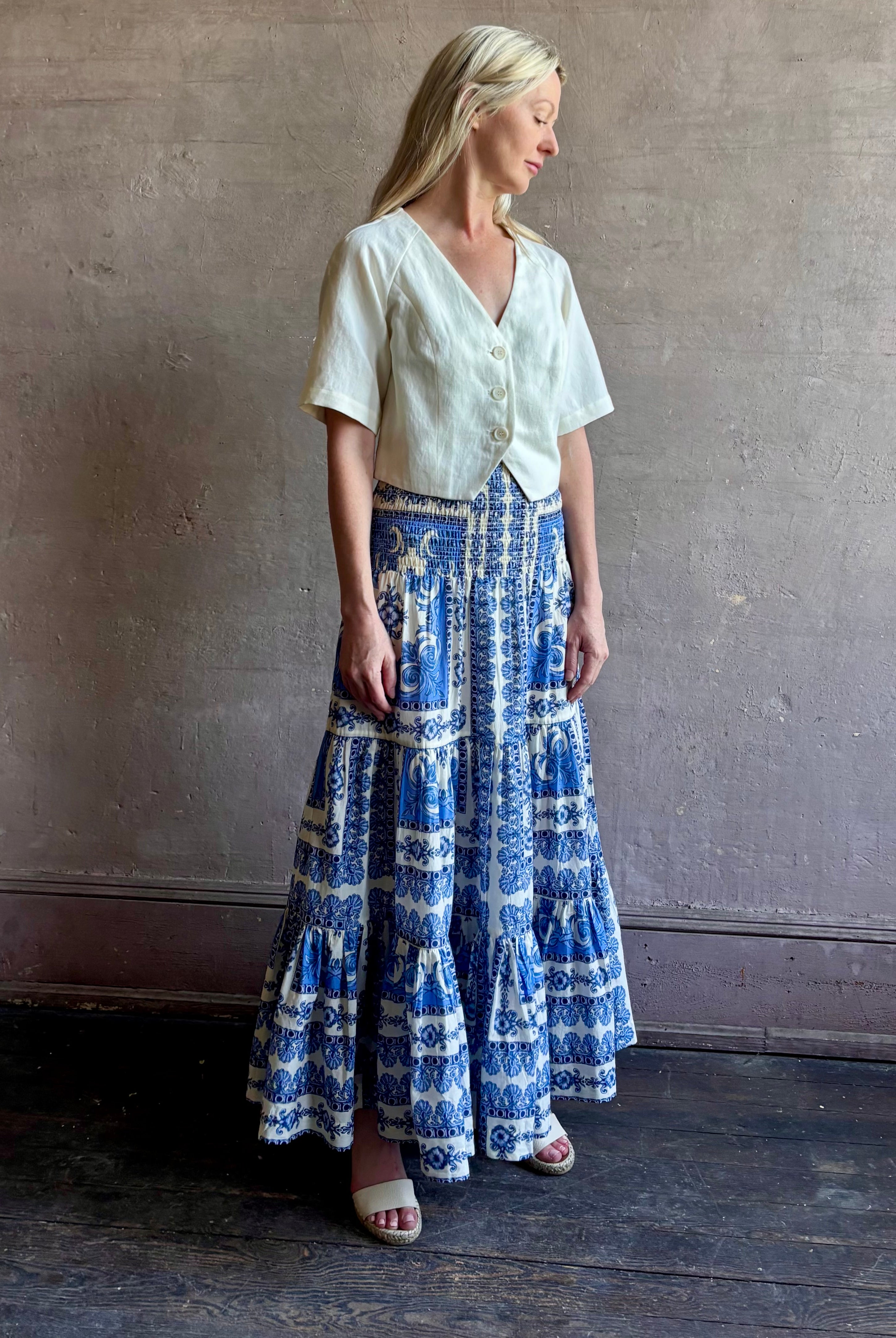 Mature woman wearing Emilia Skirt from Cara Cara rendered in the Hudson Scarf Sky blue and white print crafted from 100% cotton with shirred drop waist and ruffled tiered full skirt