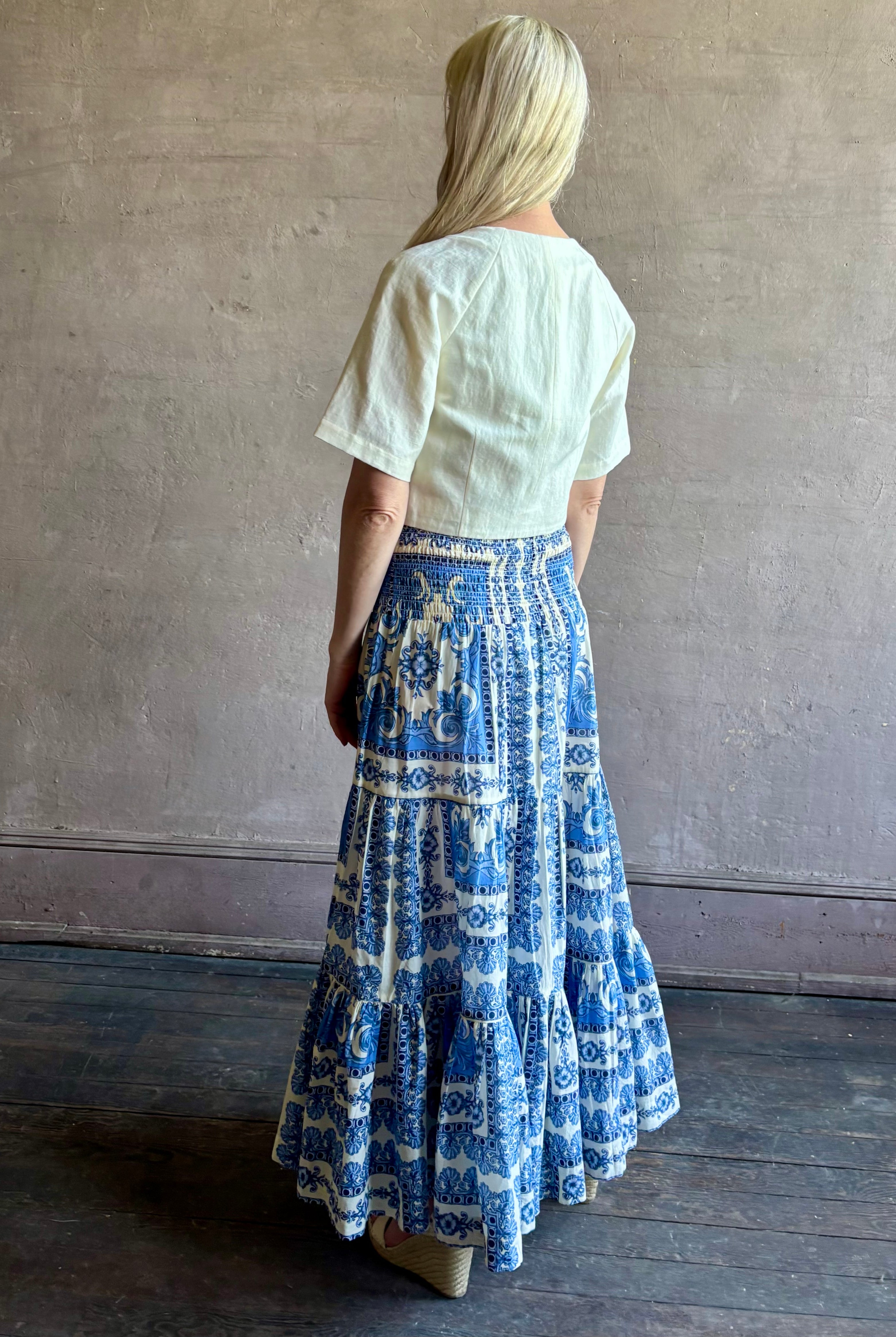 Mature woman wearing Emilia Skirt from Cara Cara rendered in the Hudson Scarf Sky blue and white print crafted from 100% cotton with shirred drop waist and ruffled tiered full skirt