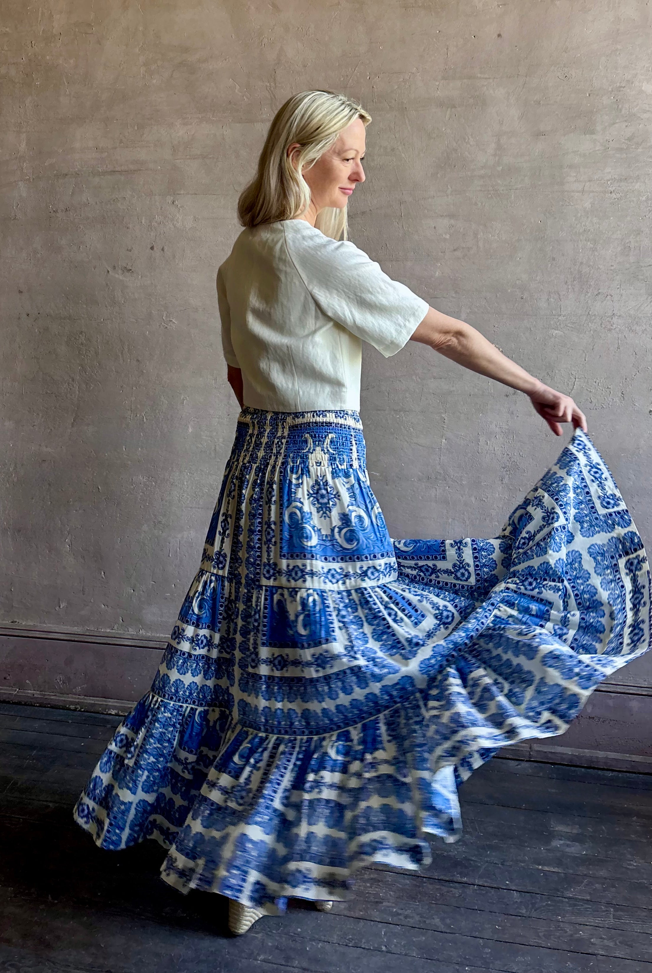 Mature woman wearing Emilia Skirt from Cara Cara rendered in the Hudson Scarf Sky blue and white print crafted from 100% cotton with shirred drop waist and ruffled tiered full skirt