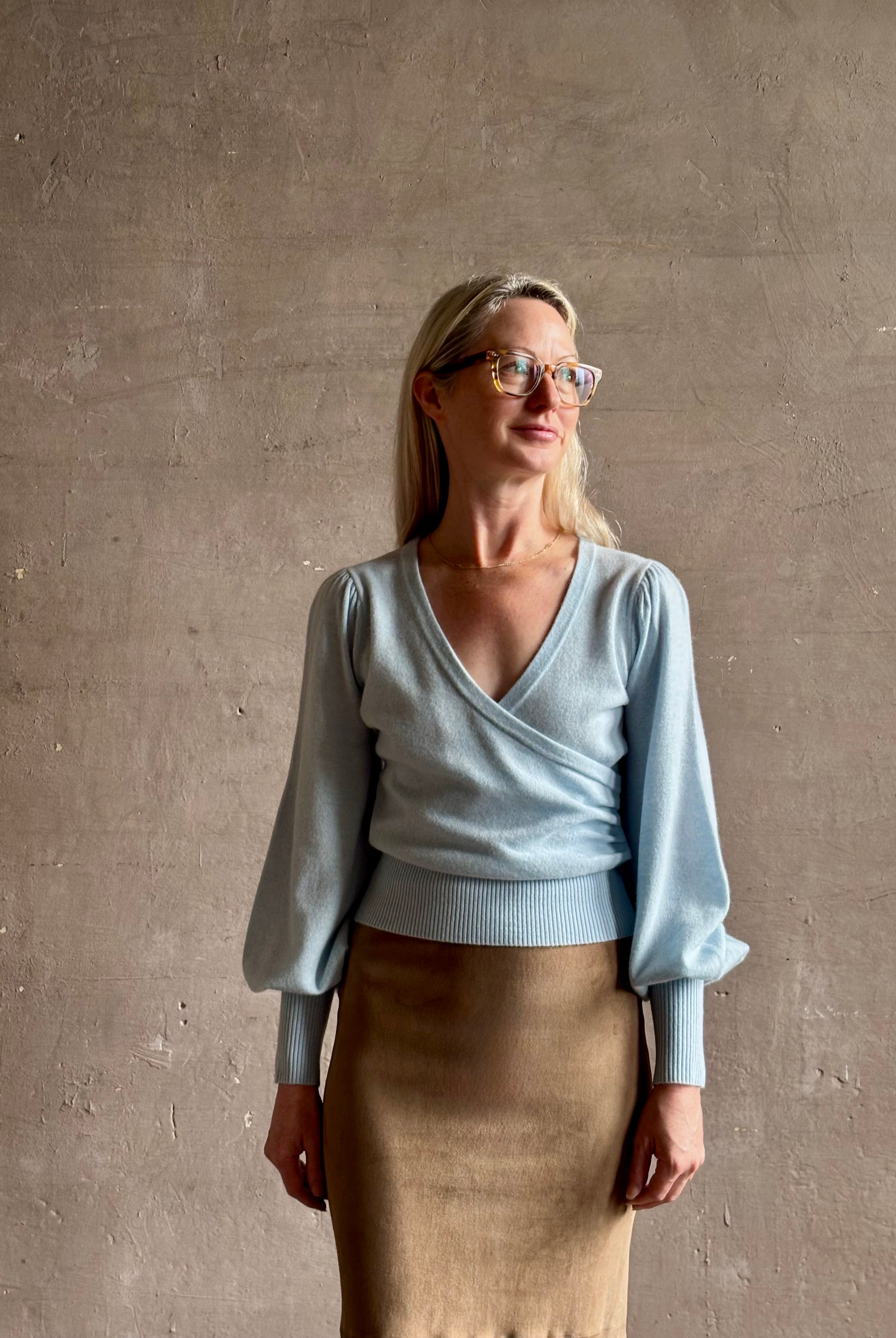 mature woman wearing designer Cara Cara wool-cashmere blend light blue wrap sweater v-neck and long sleeves