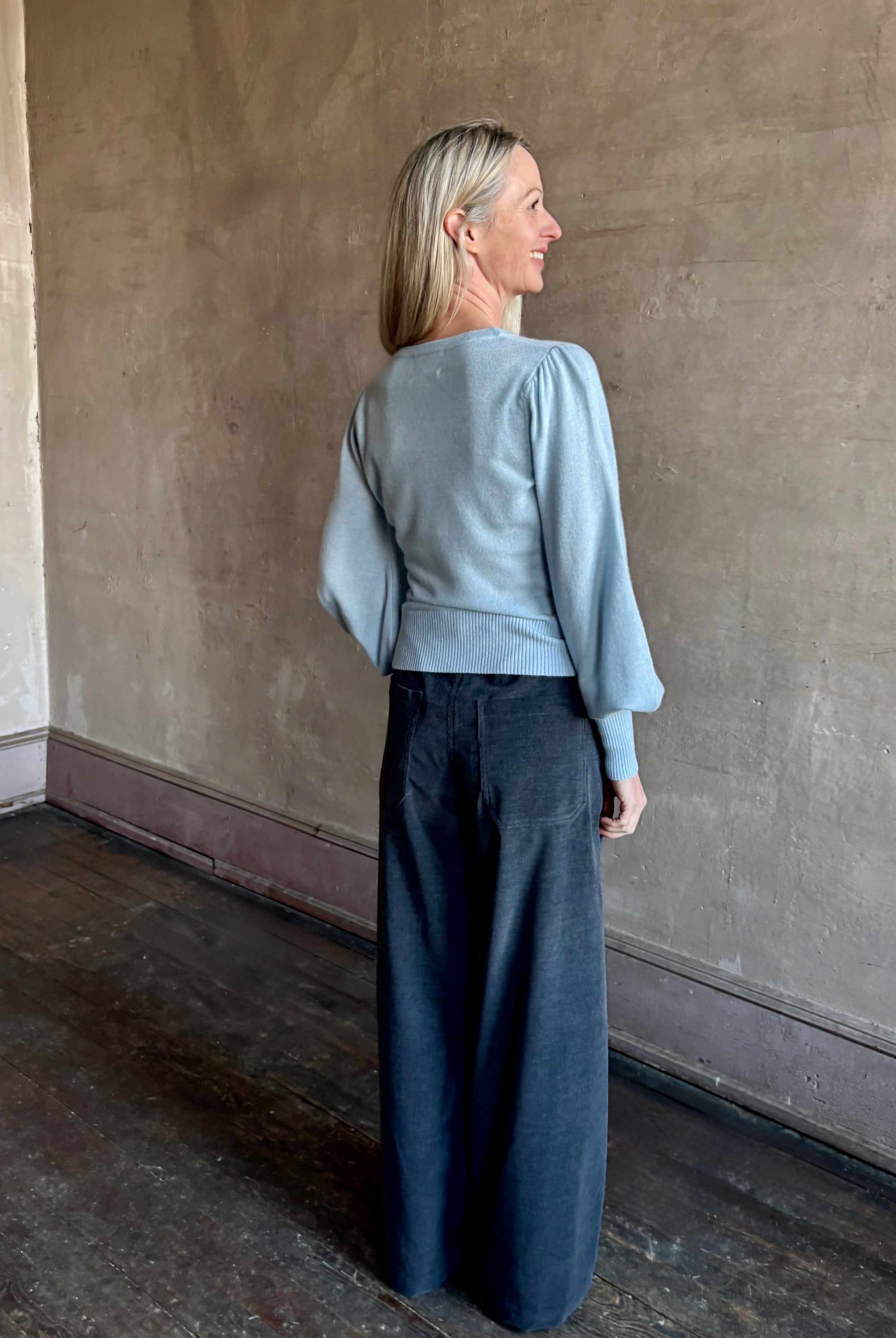 Back image of woman wearing designer Cara Cara wool-cashmere blend light blue wrap sweater with a v-neck and long sleeves
