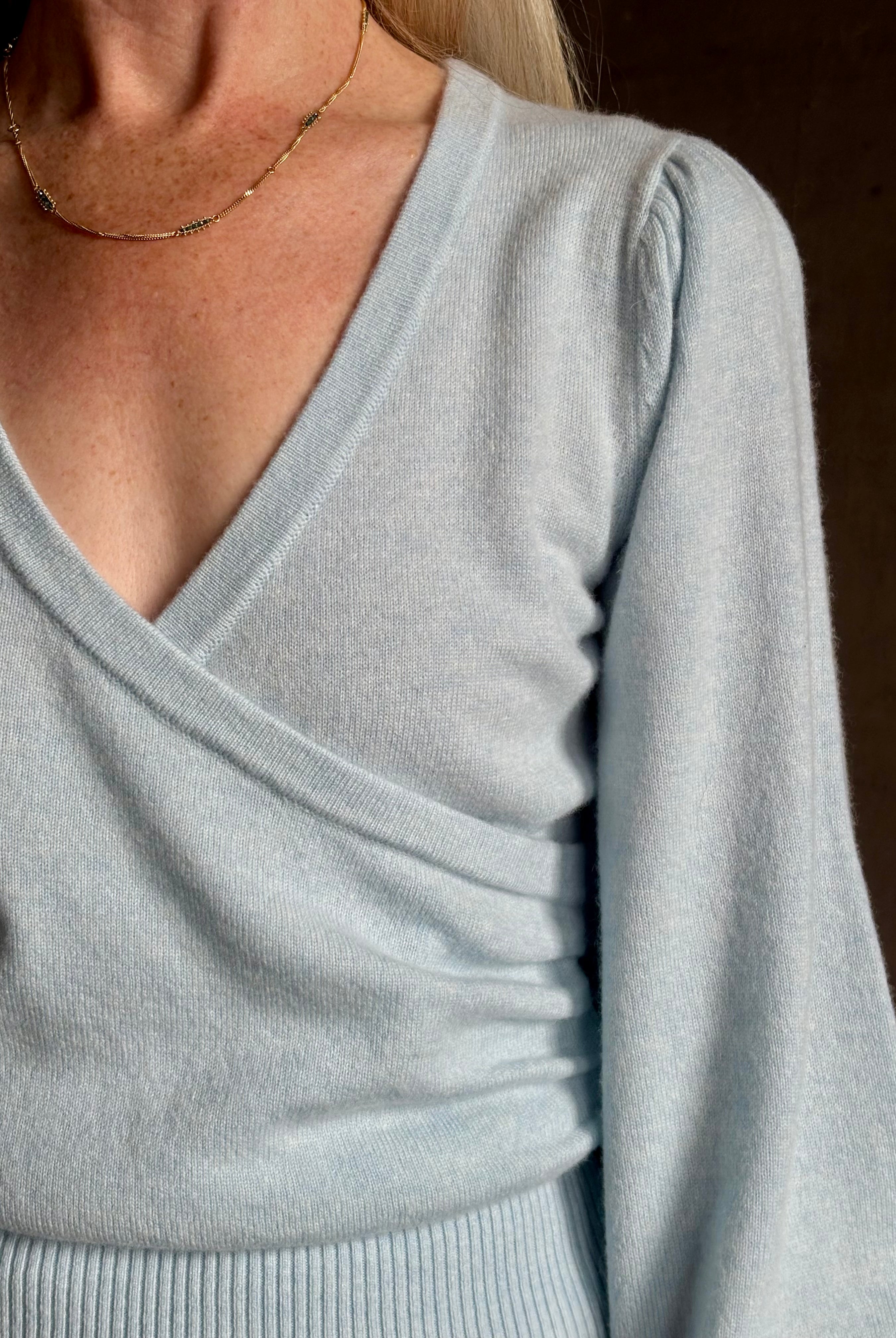 mature woman wearing designer Cara Cara wool-cashmere blend light blue wrap sweater v-neck and long sleeves