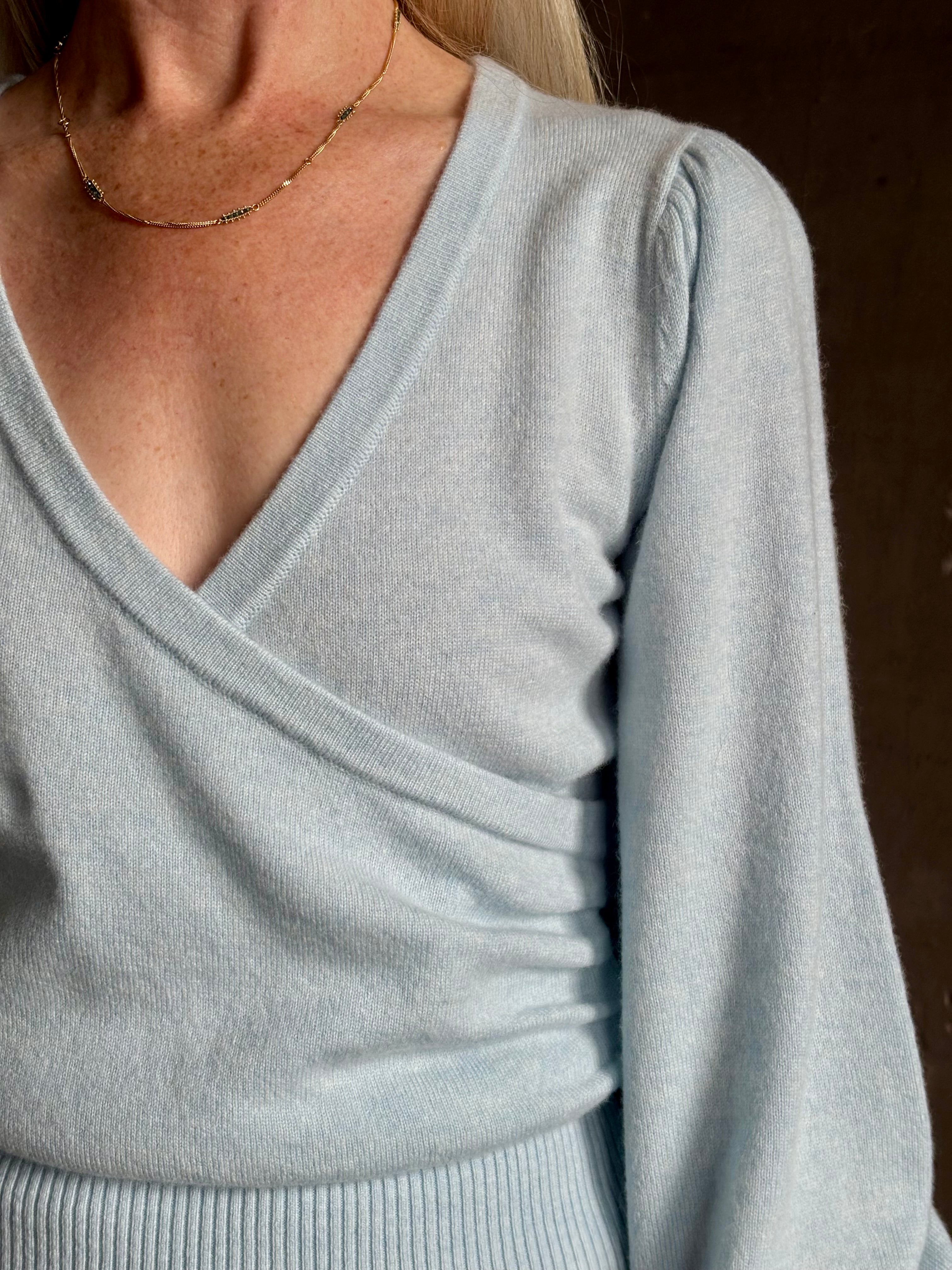 mature woman wearing designer Cara Cara wool-cashmere blend light blue wrap sweater v-neck and long sleeves