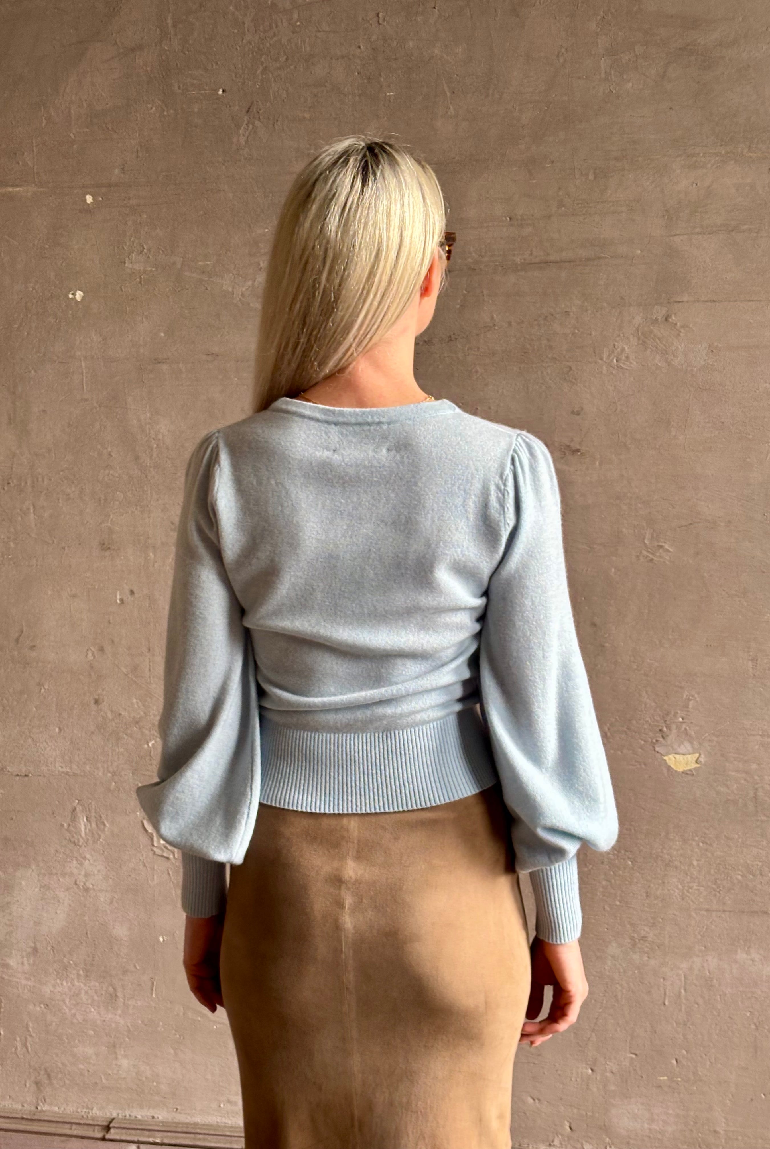 mature woman wearing designer Cara Cara wool-cashmere blend light blue wrap sweater v-neck and long sleeves