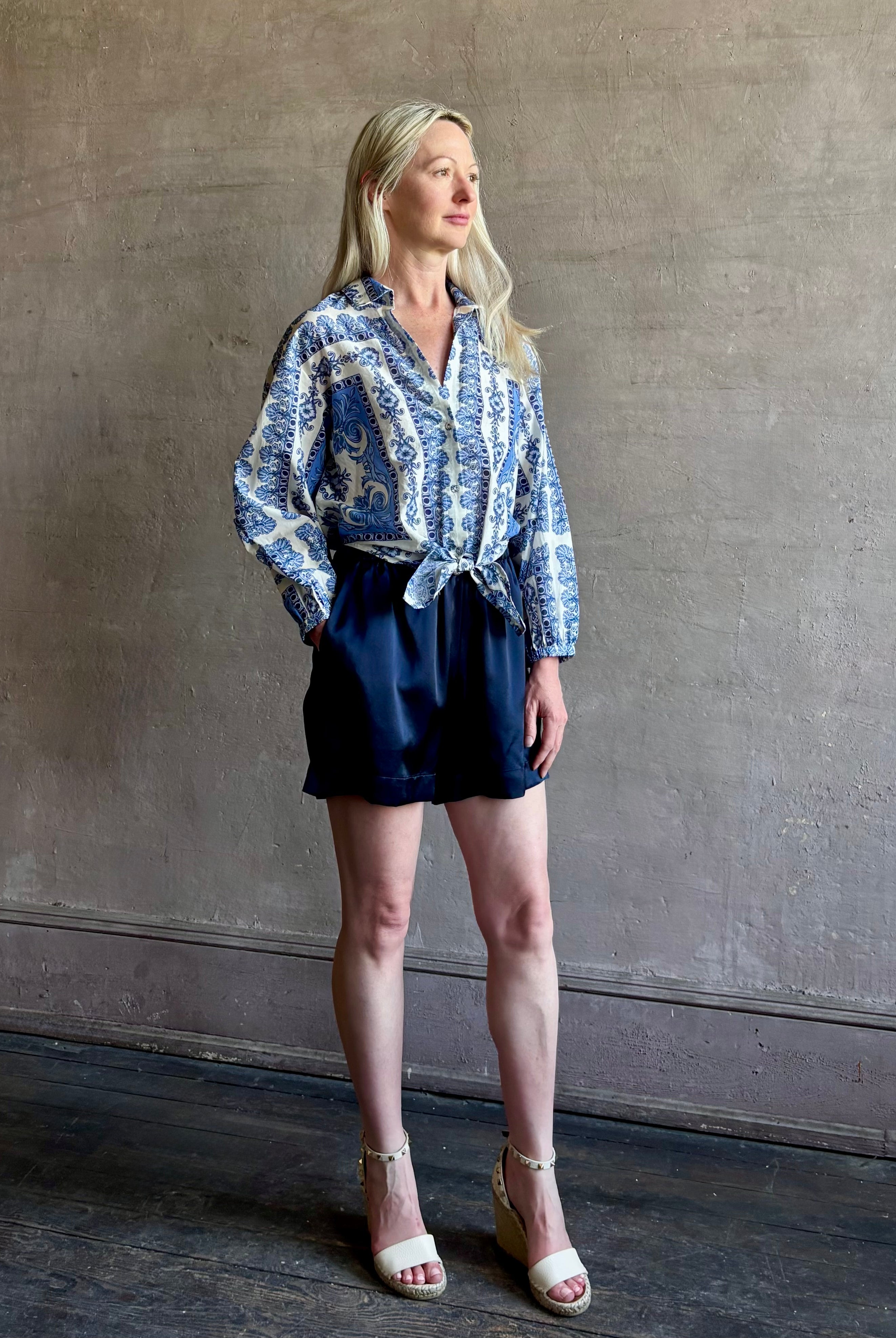 Mature woman wearing the Rumson Top from Cara Cara rendered in a blue and white Hudson Scarf Sky print and crafted from 100% cotton with long sleeves, button down v- neck and tie front cropped top