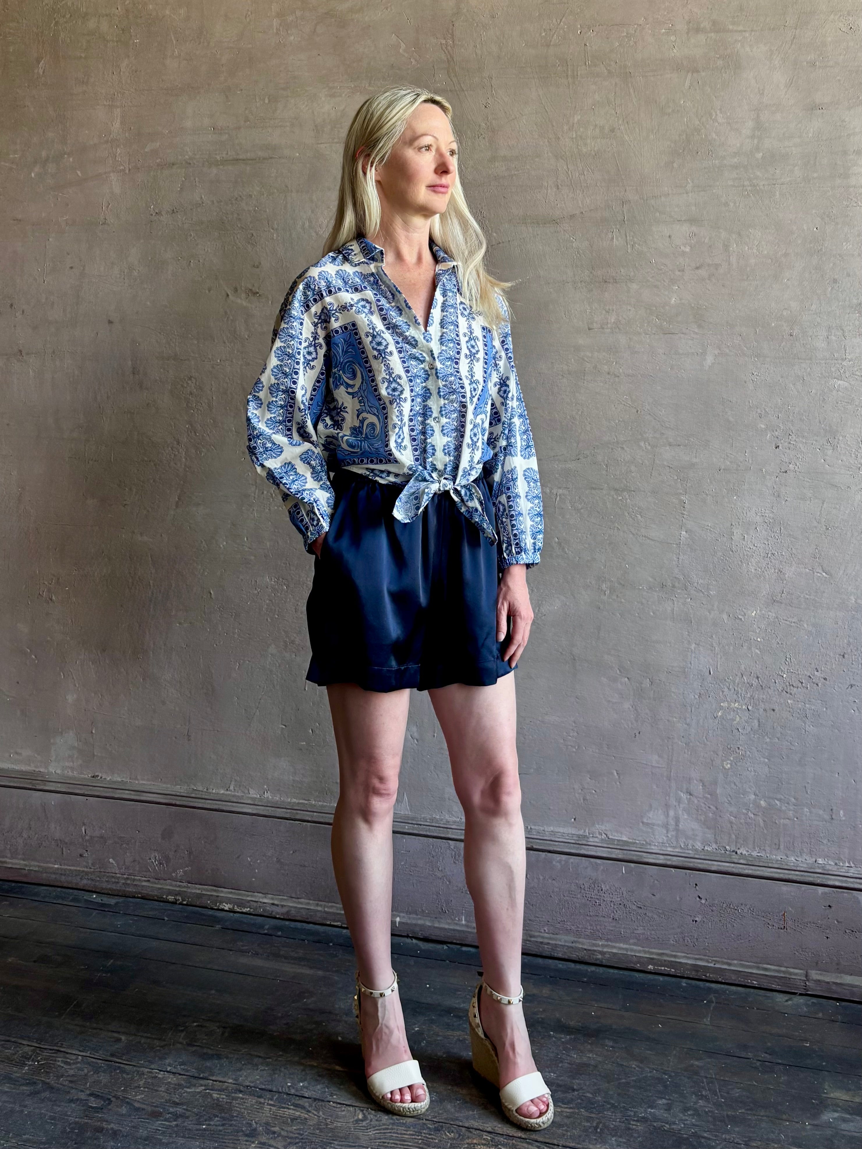 Mature woman wearing the Rumson Top from Cara Cara rendered in a blue and white Hudson Scarf Sky print and crafted from 100% cotton with long sleeves, button down v- neck and tie front cropped top