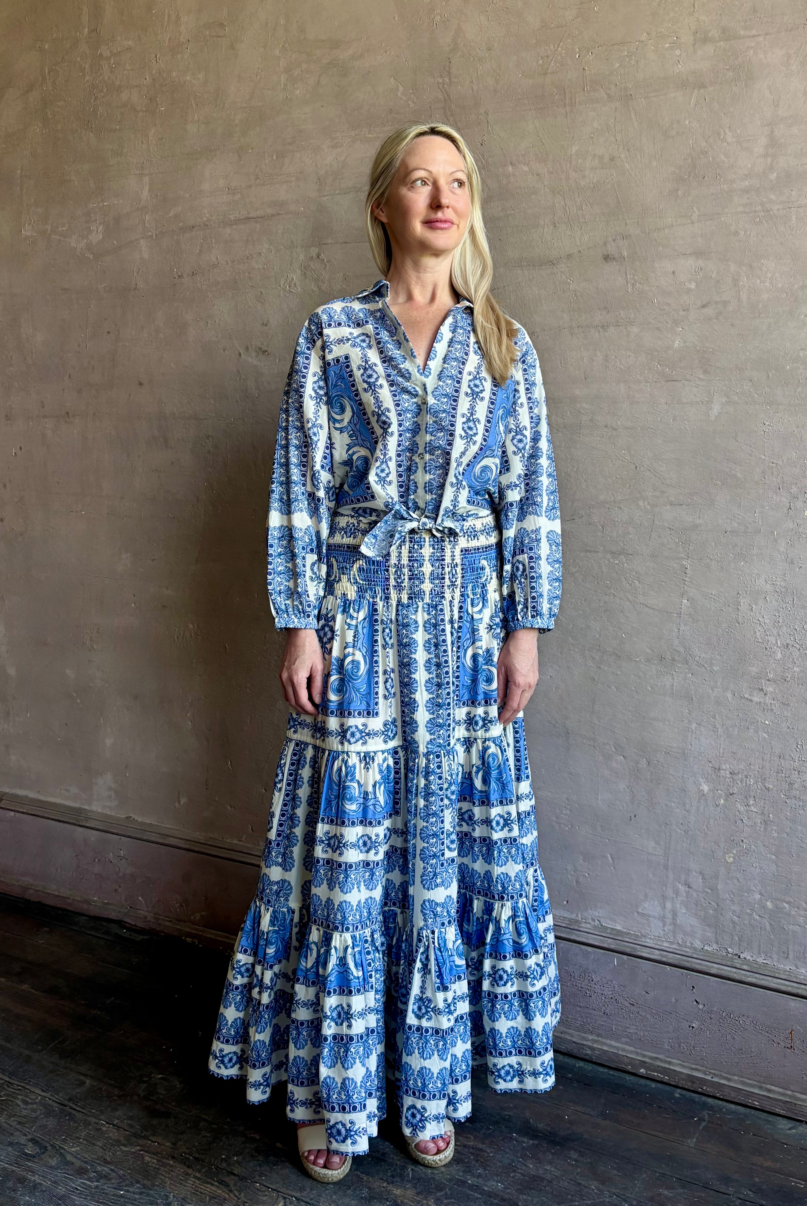 Mature woman wearing the Rumson Top from Cara Cara rendered in a blue and white Hudson Scarf Sky print and crafted from 100% cotton with long sleeves, button down v- neck and tie front cropped top