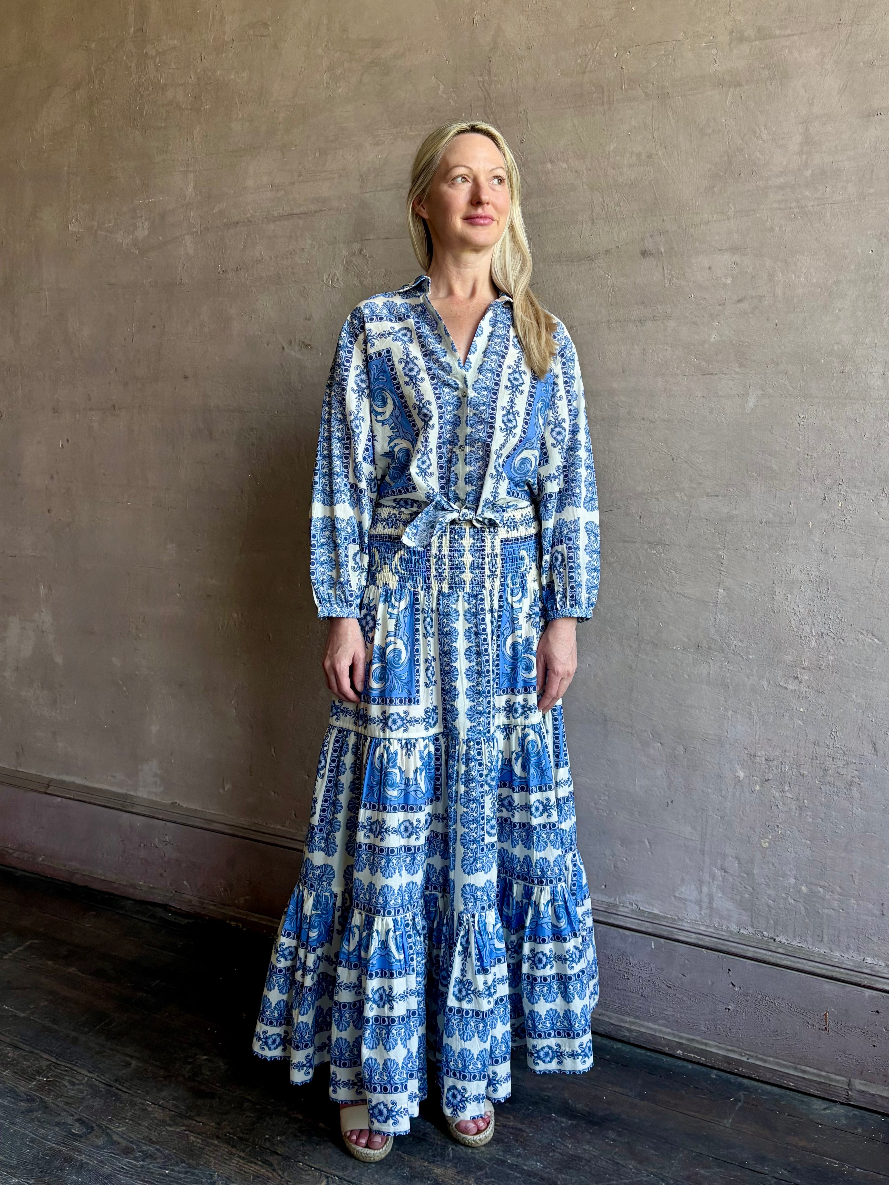 Mature woman wearing the Rumson Top from Cara Cara rendered in a blue and white Hudson Scarf Sky print and crafted from 100% cotton with long sleeves, button down v- neck and tie front cropped top