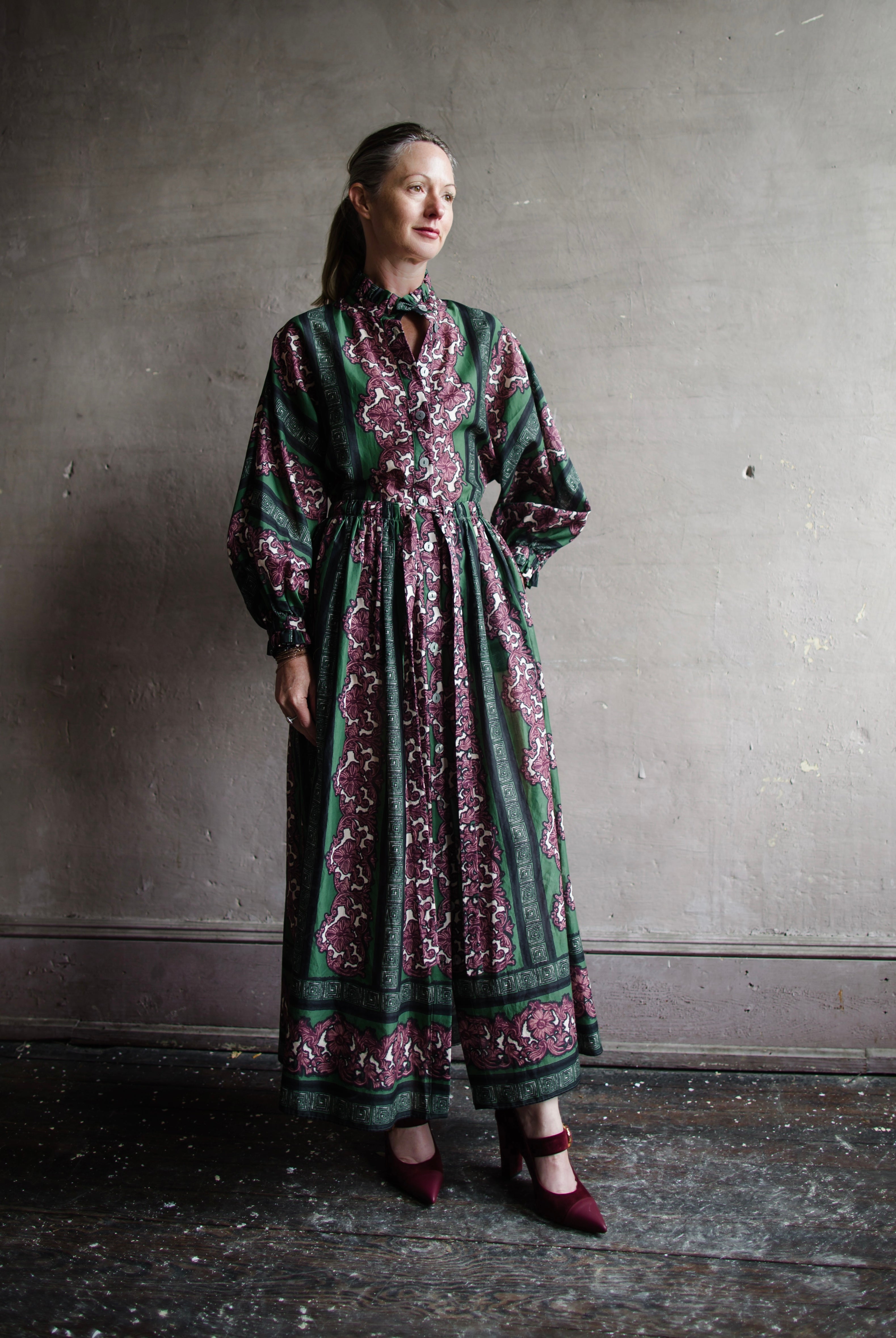 Image features woman wearing Cara Cara Beatrice Dress. This dress is full length with long sleeves and a drawstring waist.