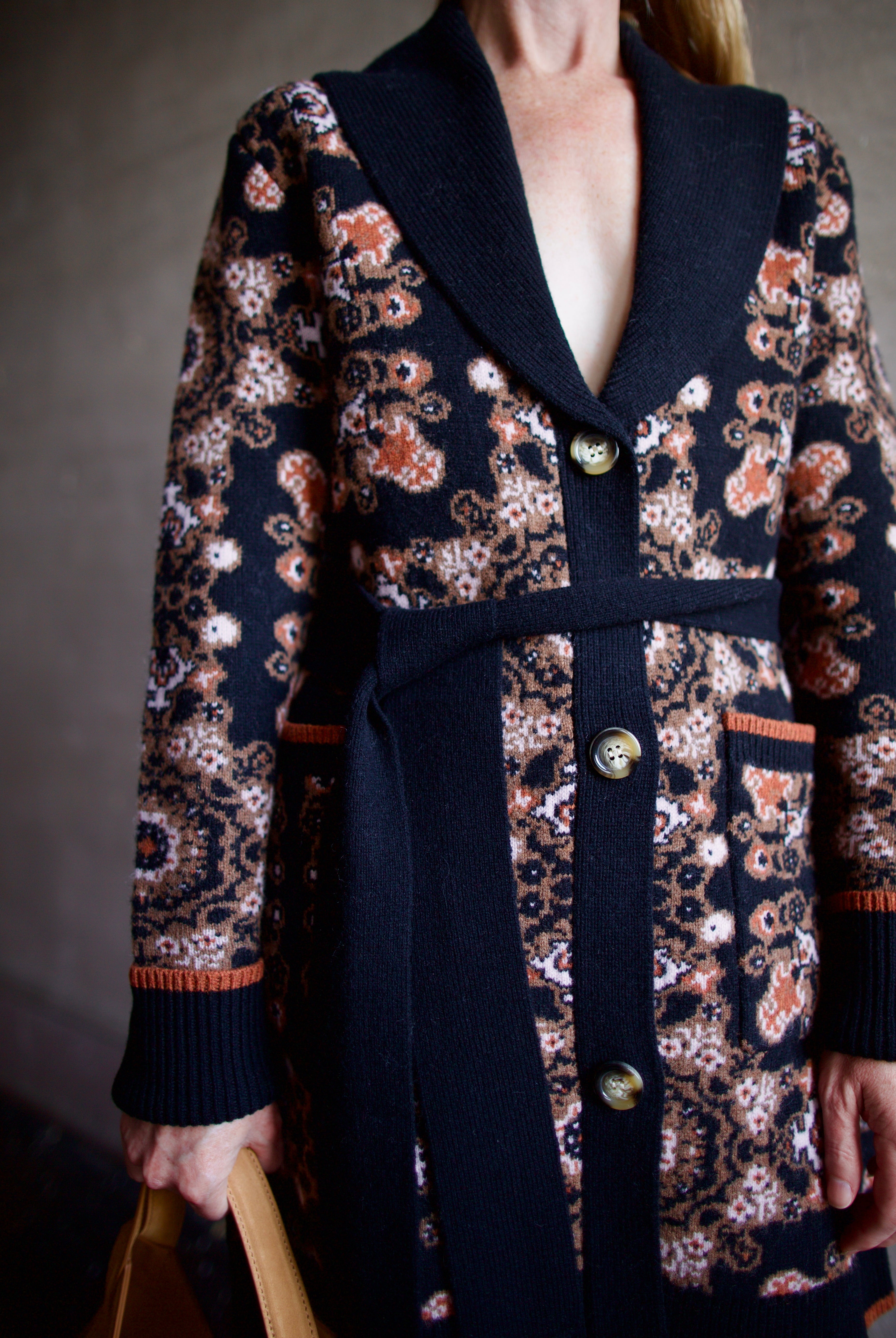 Image featuring a woman wearing the Laney cardigan by Cara Cara with ribbed collar, a tie waist, front pockets, and mid thigh length true to size fit.