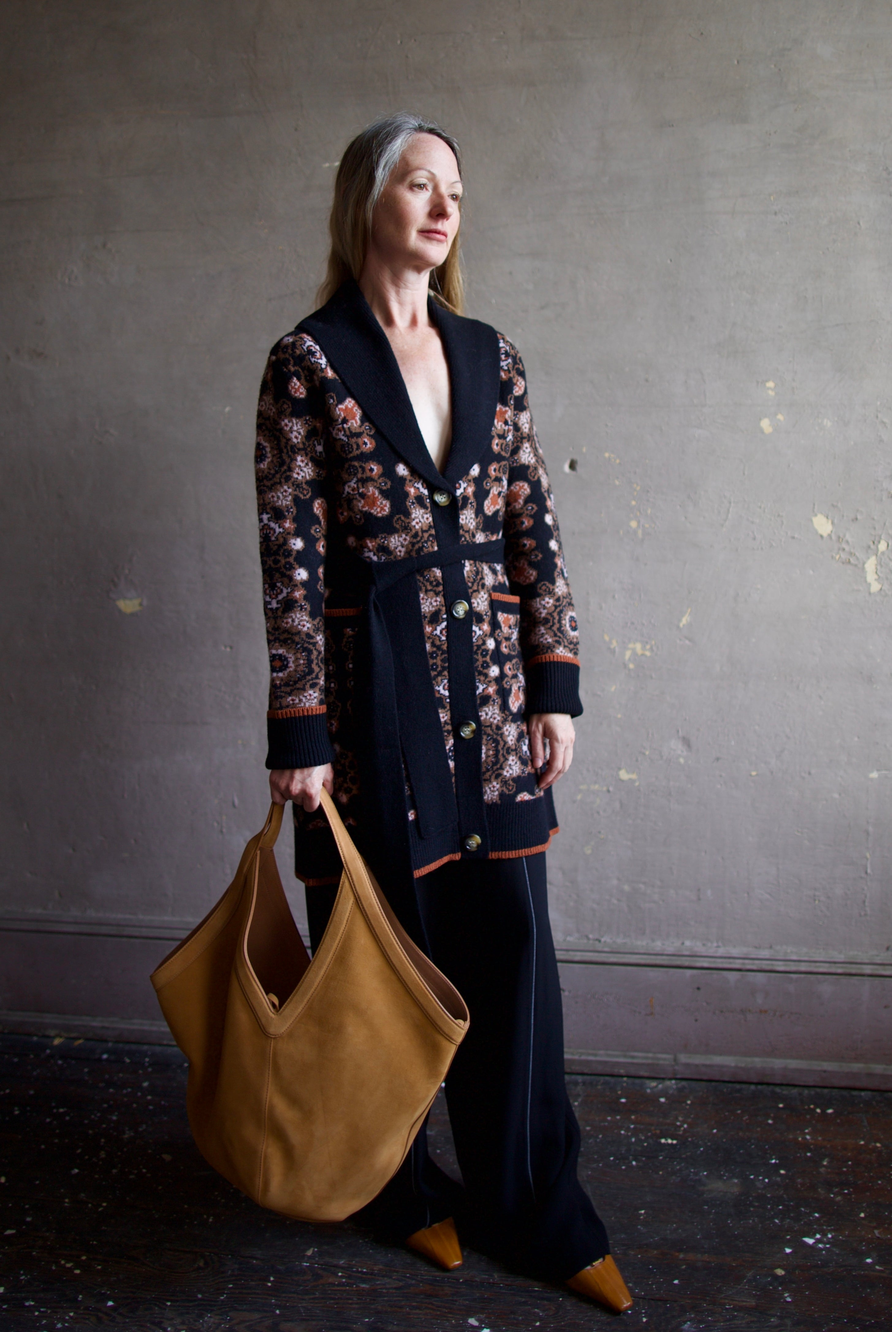 Image featuring a woman wearing the Laney cardigan by Cara Cara with ribbed collar, a tie waist, front pockets, and mid thigh length true to size fit.