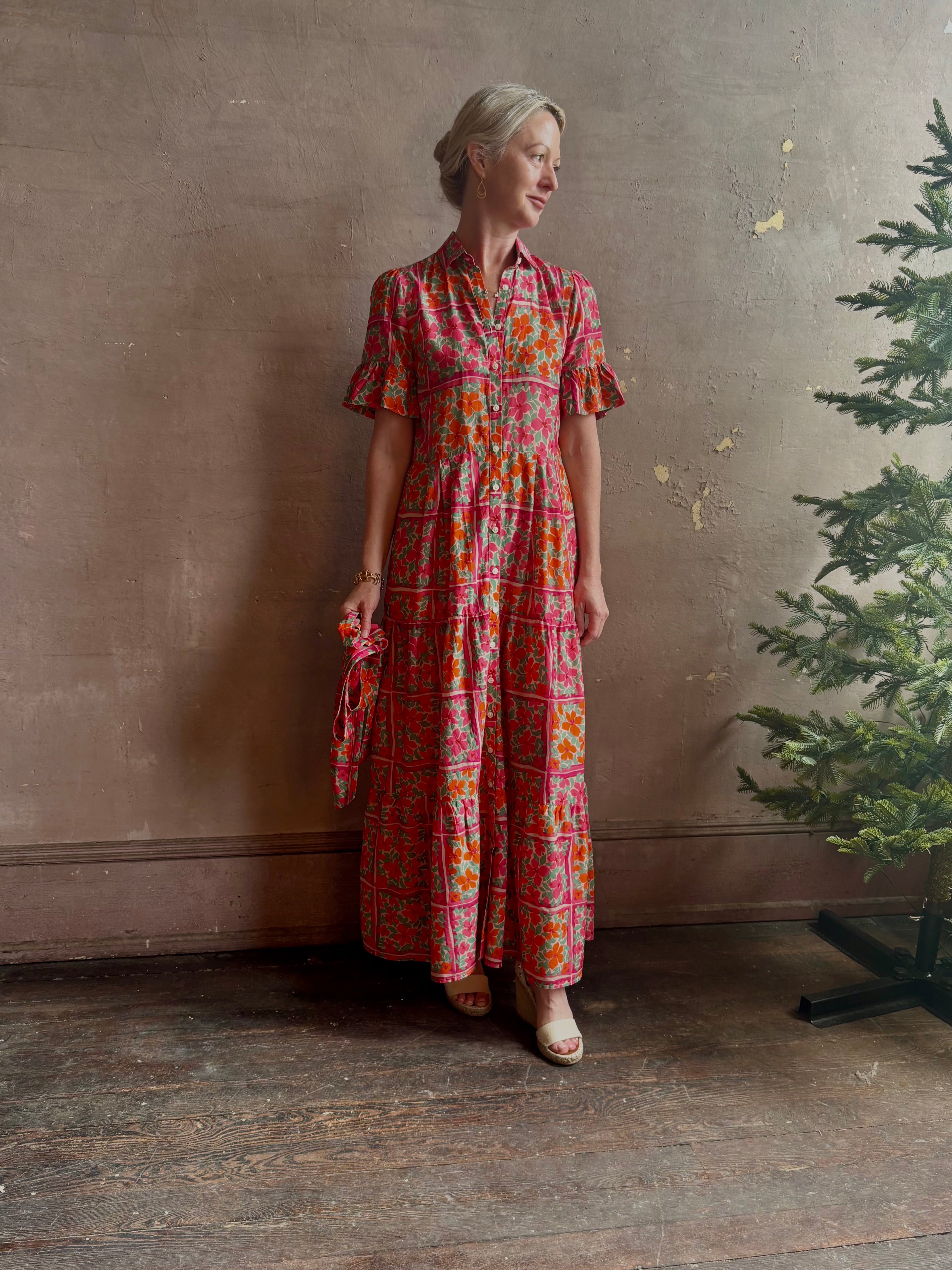 Mature woman wearing Martine maxi Dress from Trovata rendered in the Botanic Tile pink and orange floral print and crafted from a luxurious blend of cotton and silk with button front, collar, short sleeves and matching optional self tile belt