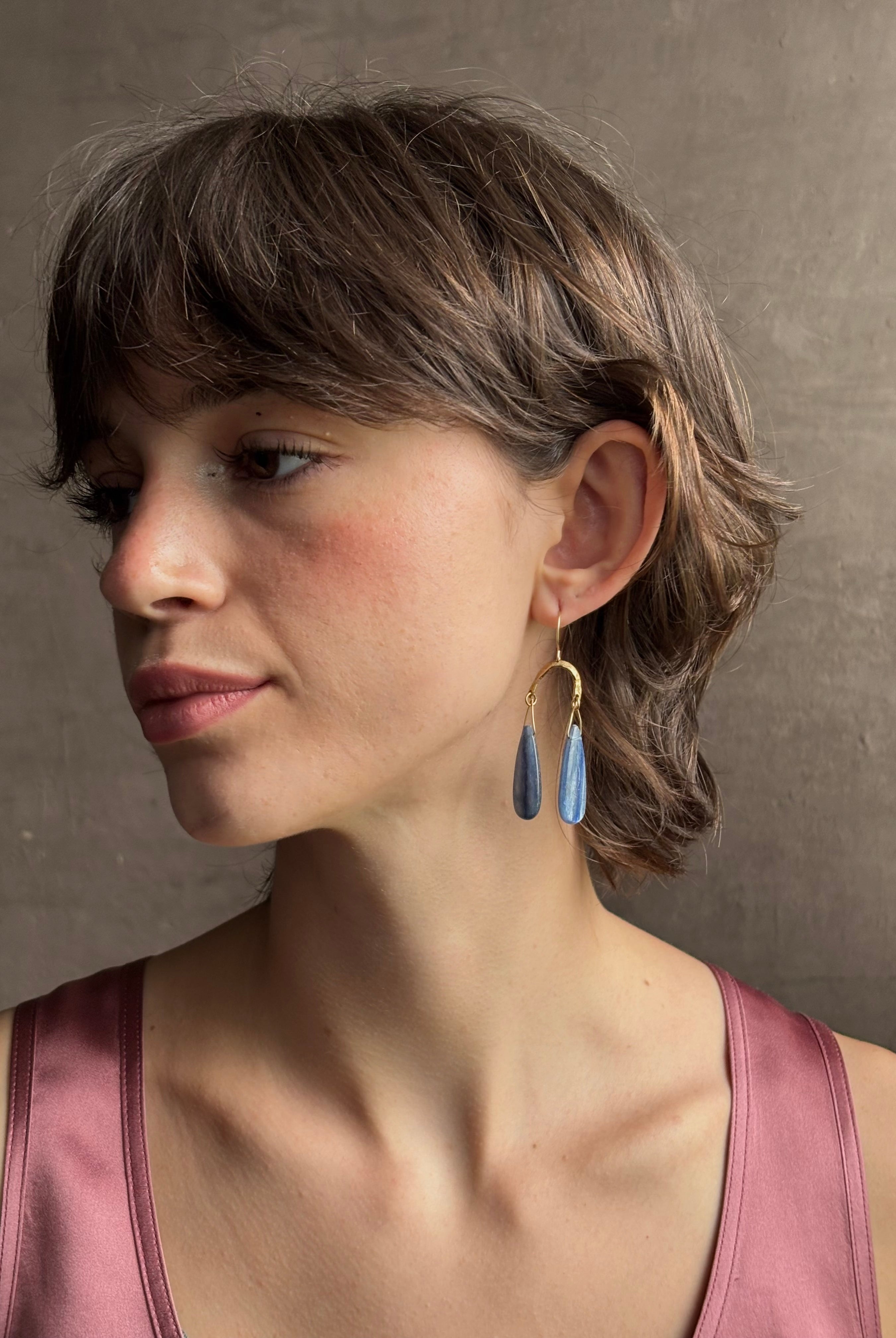 Woman wearing Delta Earrings from New York fine jewelry artist Emilie Shapiro with dangling teardrop shaped polished kyanite and warm textured half circle brass dangle gracefully from handmade gold filled earring wires