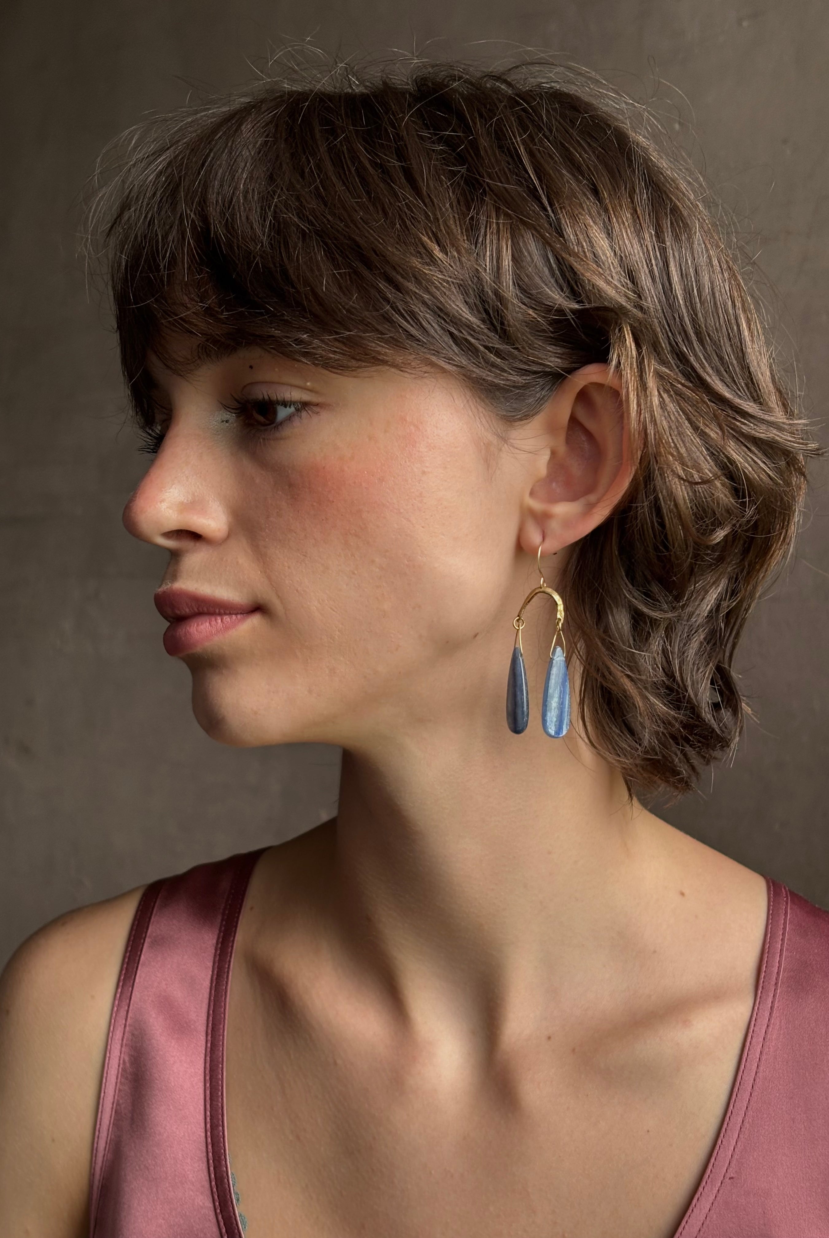 Woman wearing Delta Earrings from New York fine jewelry artist Emilie Shapiro with dangling teardrop shaped polished kyanite and warm textured half circle brass dangle gracefully from handmade gold filled earring wires