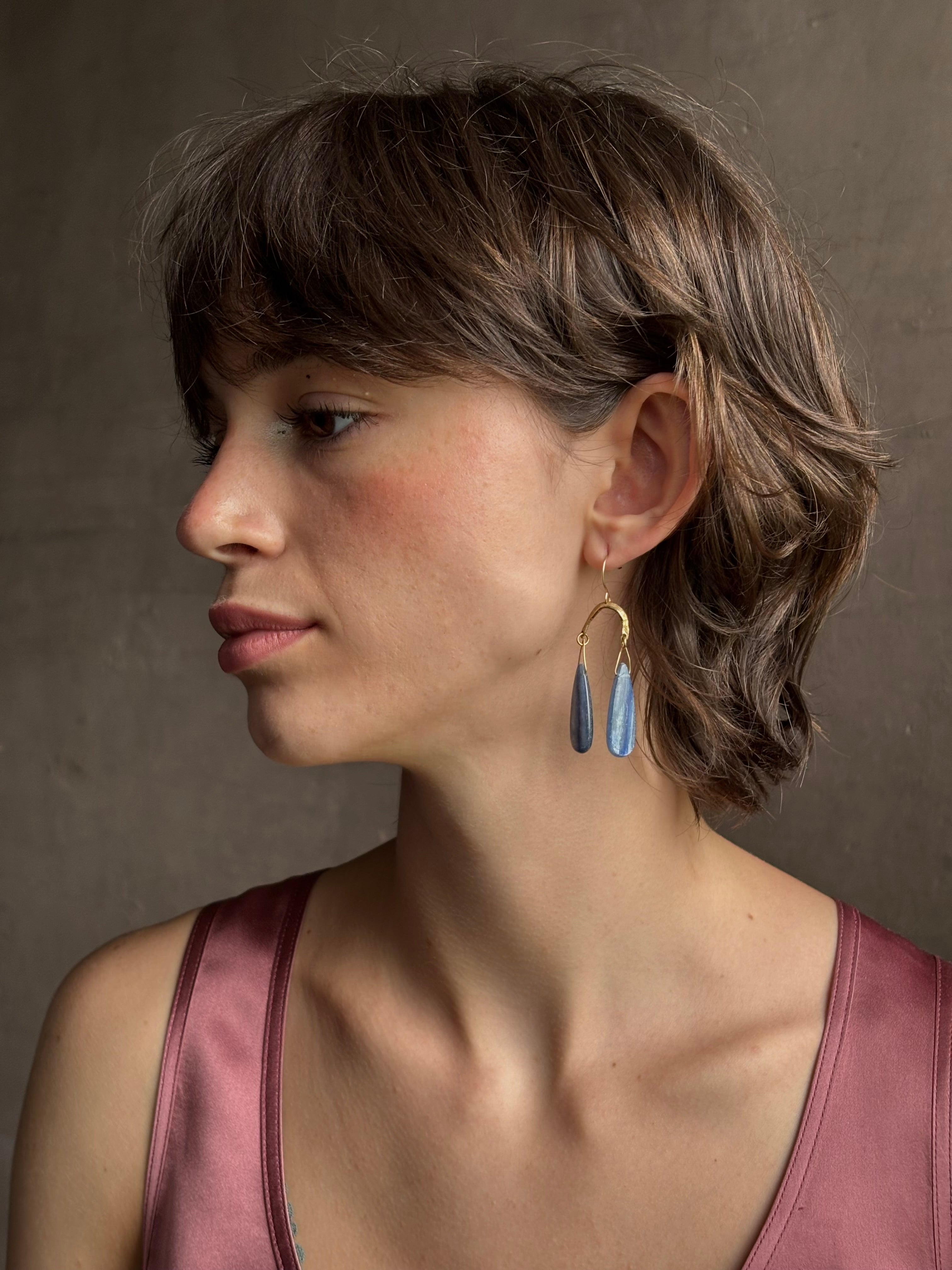 Woman wearing Delta Earrings from New York fine jewelry artist Emilie Shapiro with dangling teardrop shaped polished kyanite and warm textured half circle brass dangle gracefully from handmade gold filled earring wires