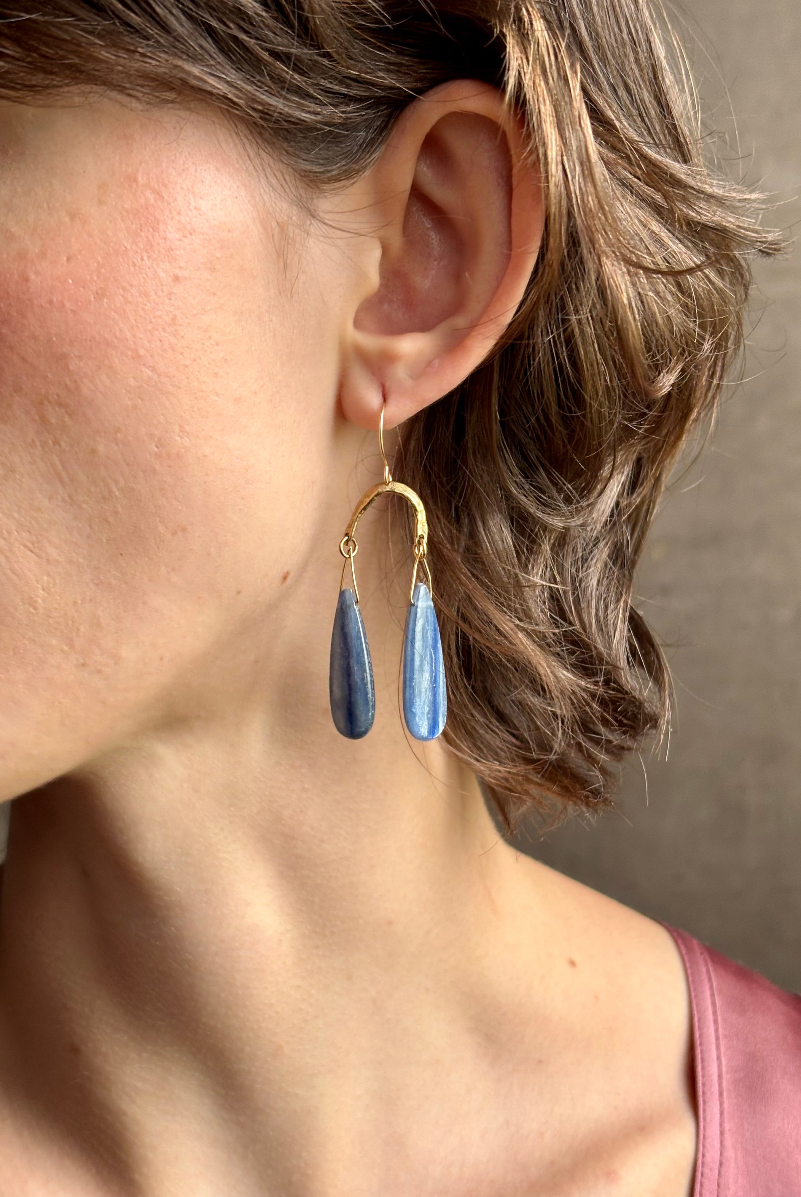 Woman wearing Delta Earrings from New York fine jewelry artist Emilie Shapiro with dangling teardrop shaped polished kyanite and warm textured half circle brass dangle gracefully from handmade gold filled earring wires