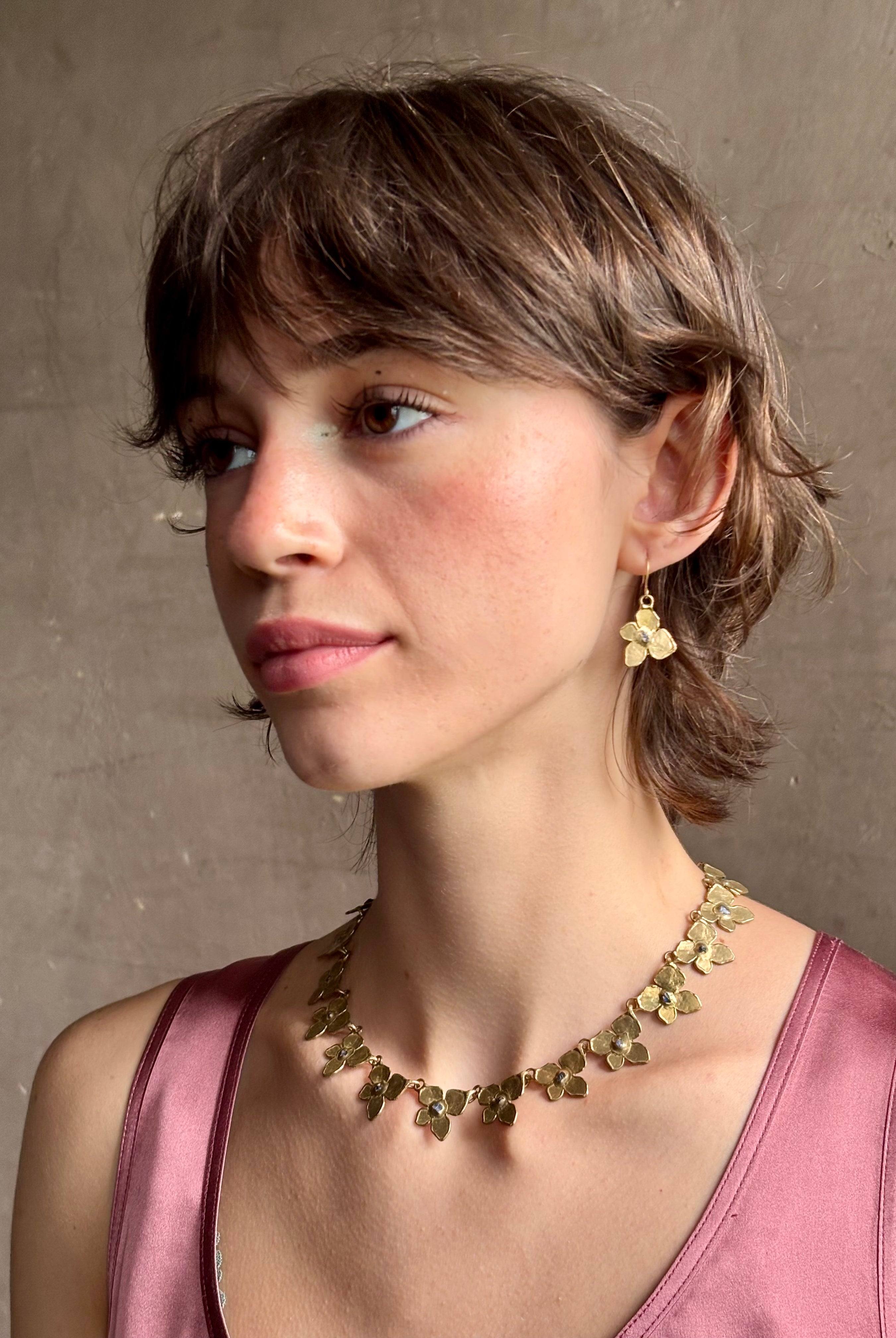 Woman wearing Hydrangea Collar Necklace from New Yok fine jewelry designer Emilie Shapiro is a statement piece with Natural blue sapphires are individually embedded in warm, textured brass with artful exploration of form and movement handcrafted in USA