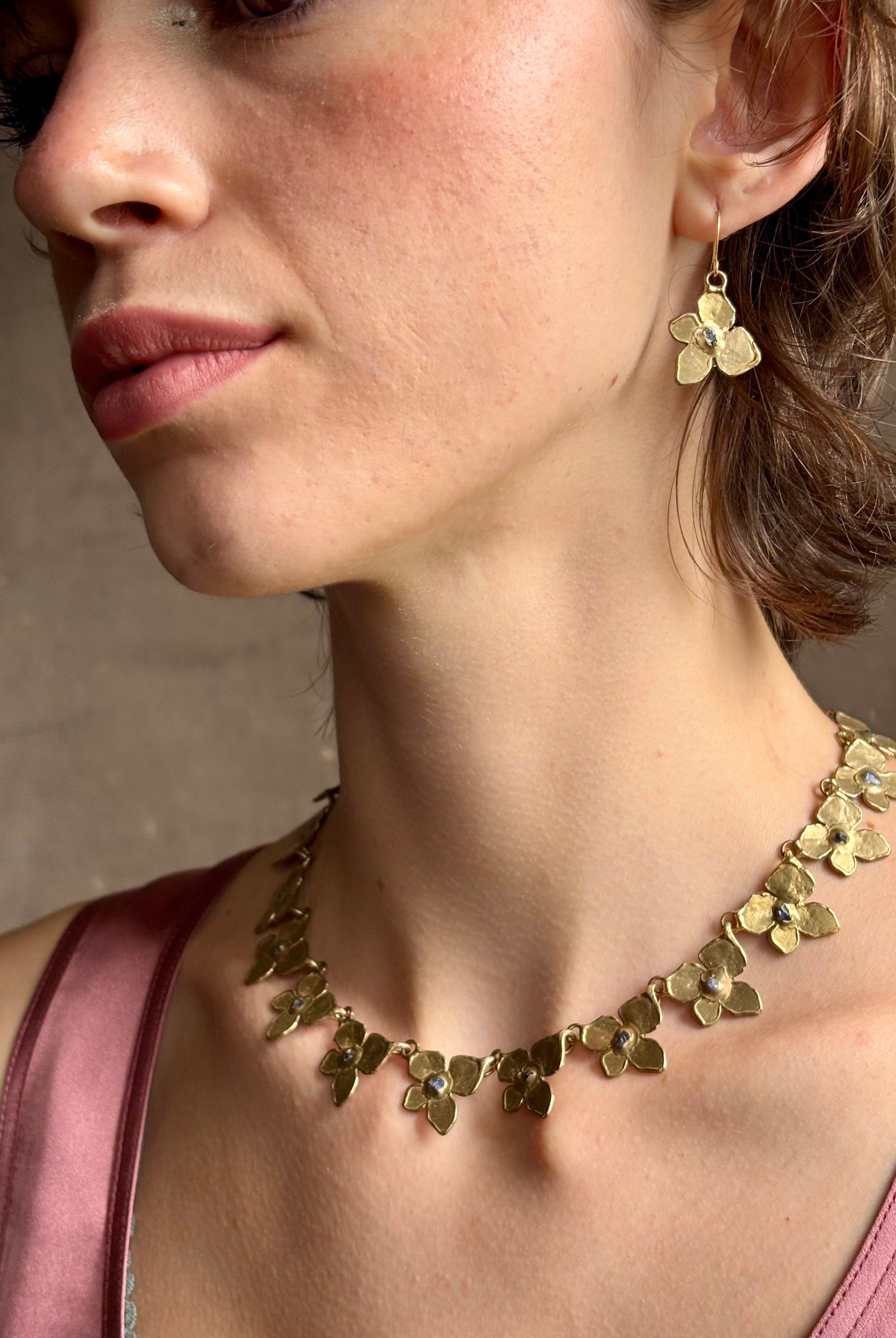 Woman wearing Hydrangea Collar Necklace from New Yok fine jewelry designer Emilie Shapiro is a statement piece with Natural blue sapphires are individually embedded in warm, textured brass with artful exploration of form and movement handcrafted in USA