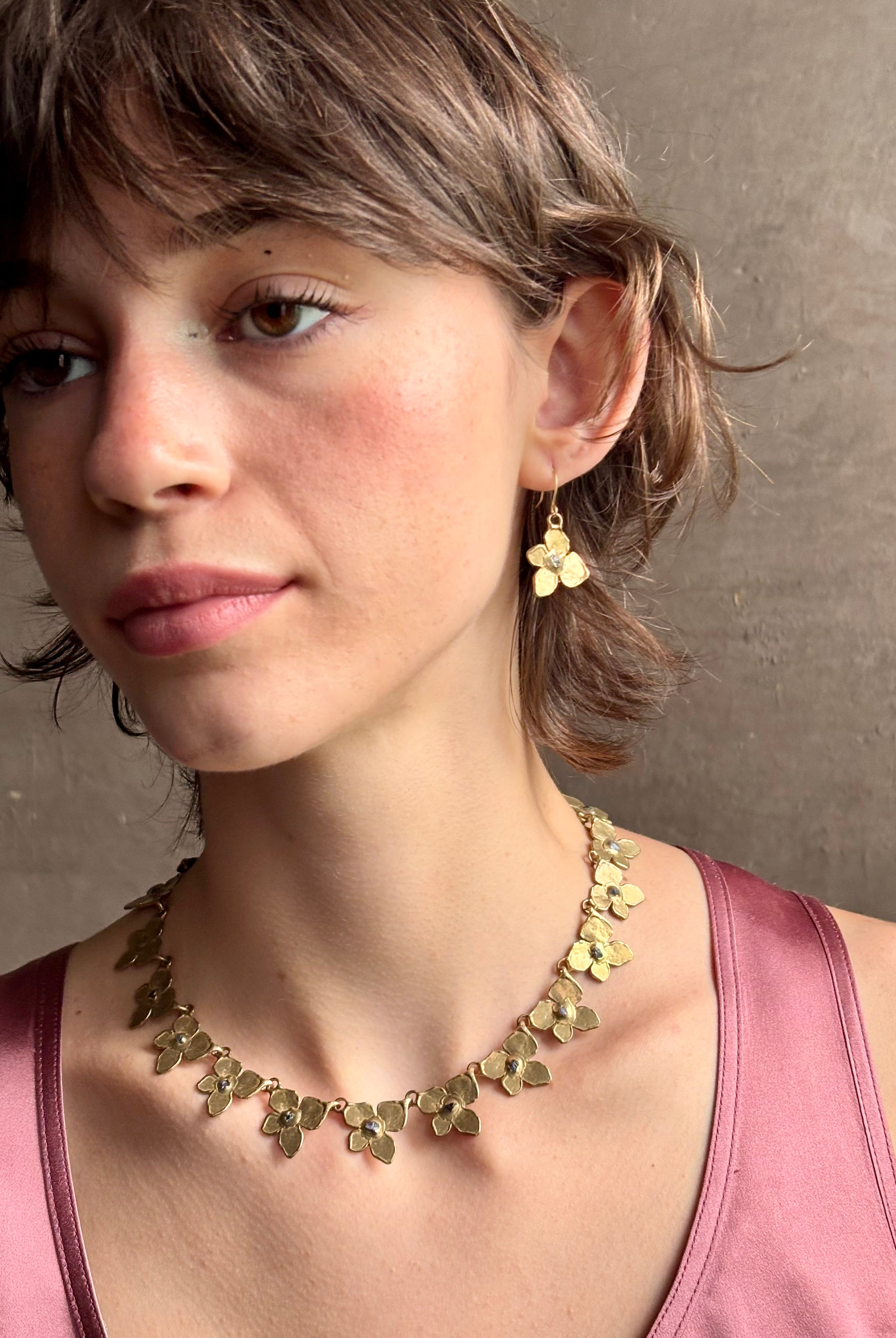 Woman wearing Hydrangea Collar Necklace from New Yok fine jewelry designer Emilie Shapiro is a statement piece with Natural blue sapphires are individually embedded in warm, textured brass with artful exploration of form and movement handcrafted in USA