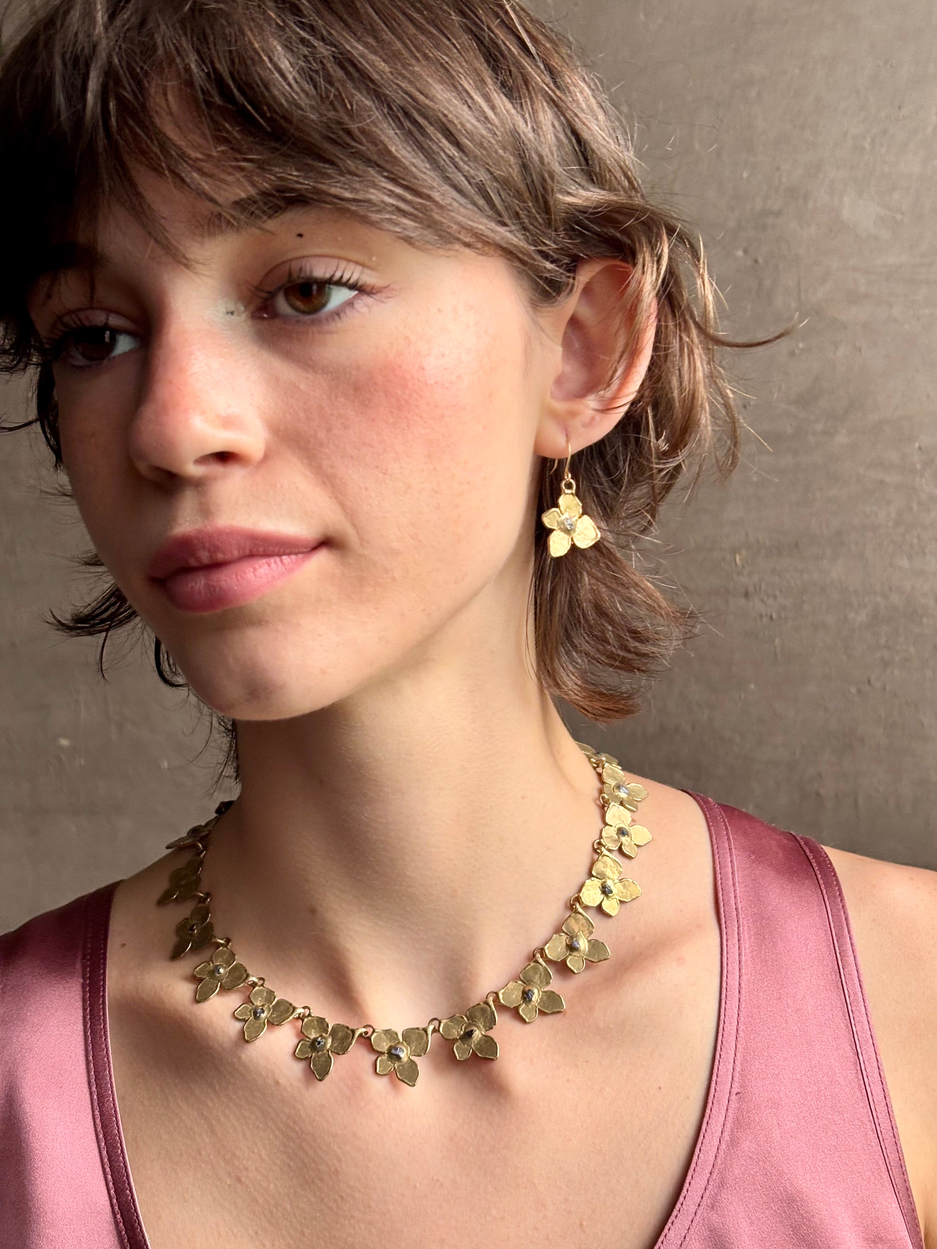 Woman wearing Hydrangea Collar Necklace from New Yok fine jewelry designer Emilie Shapiro is a statement piece with Natural blue sapphires are individually embedded in warm, textured brass with artful exploration of form and movement handcrafted in USA