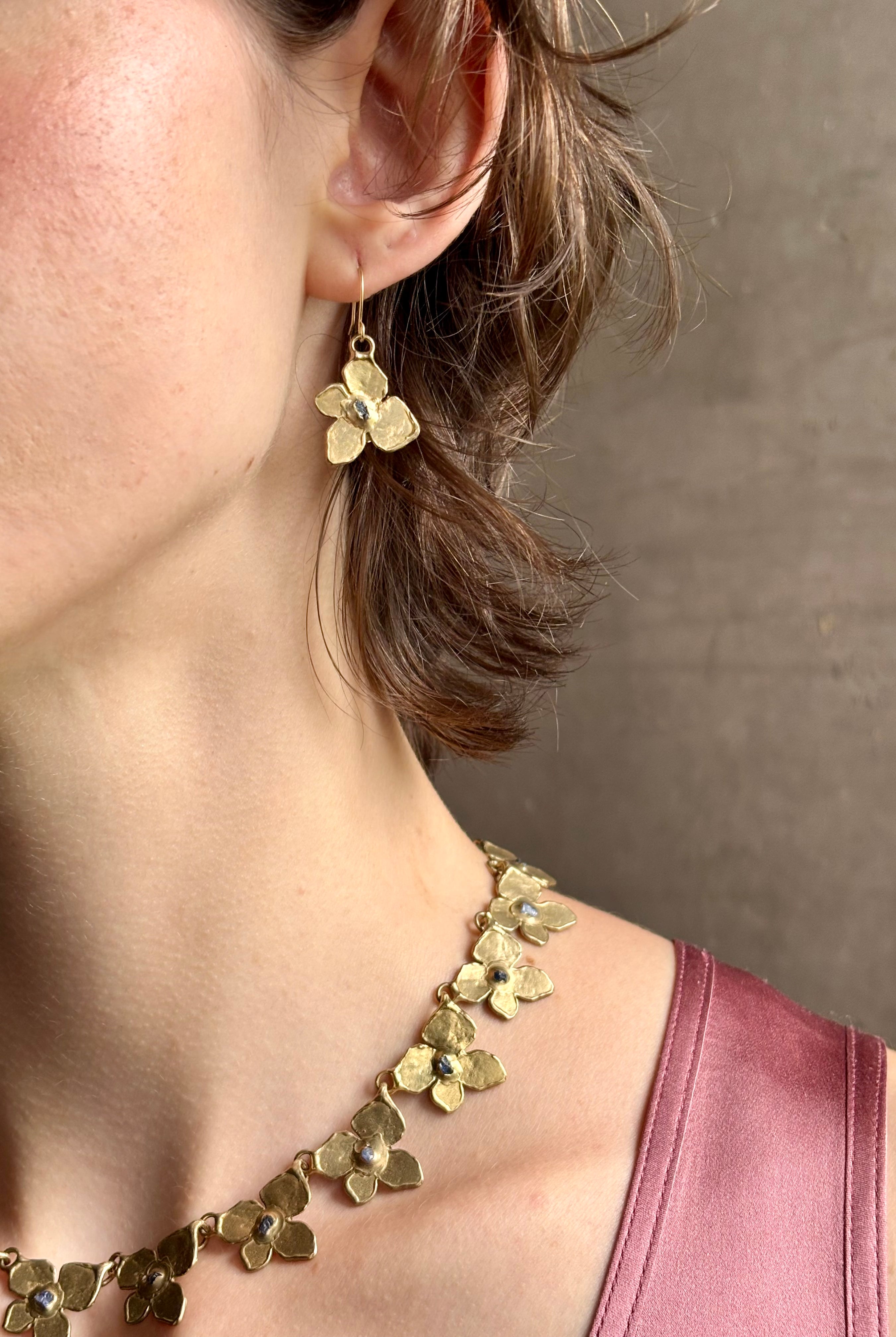 Woman wearing Hydrangea Earrings from New York fine jewelry artist Emilie Shapiro are botanically inspired with Raw sapphires embedded in warm, textured brass dangle from gold wire hoops handcrafted in USA