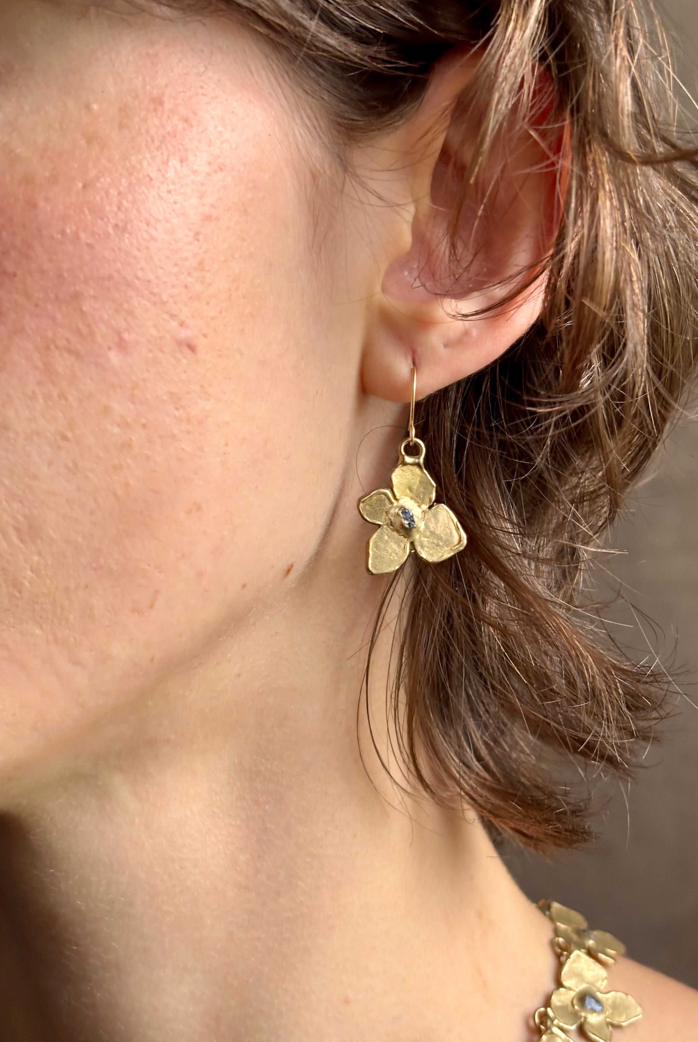 Woman wearing Hydrangea Earrings from New York fine jewelry artist Emilie Shapiro are botanically inspired with Raw sapphires embedded in warm, textured brass dangle from gold wire hoops handcrafted in USA