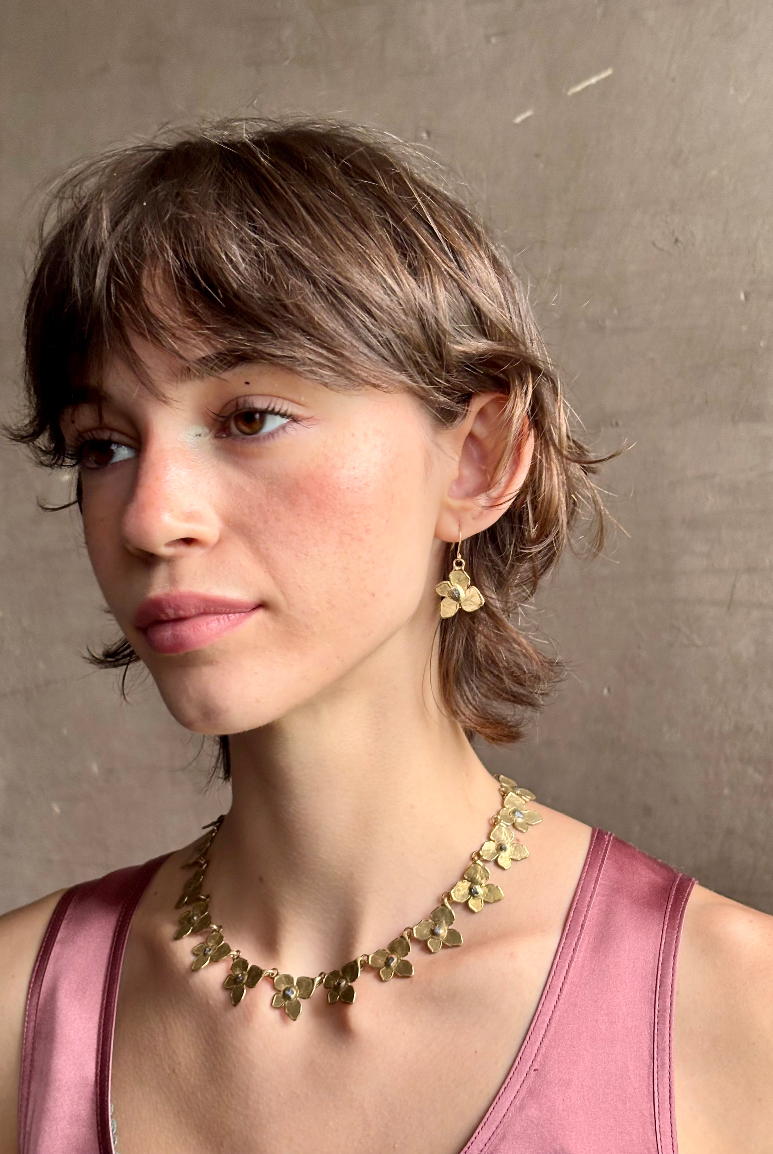 Woman wearing Hydrangea Earrings from New York fine jewelry artist Emilie Shapiro are botanically inspired with Raw sapphires embedded in warm, textured brass dangle from gold wire hoops handcrafted in USA