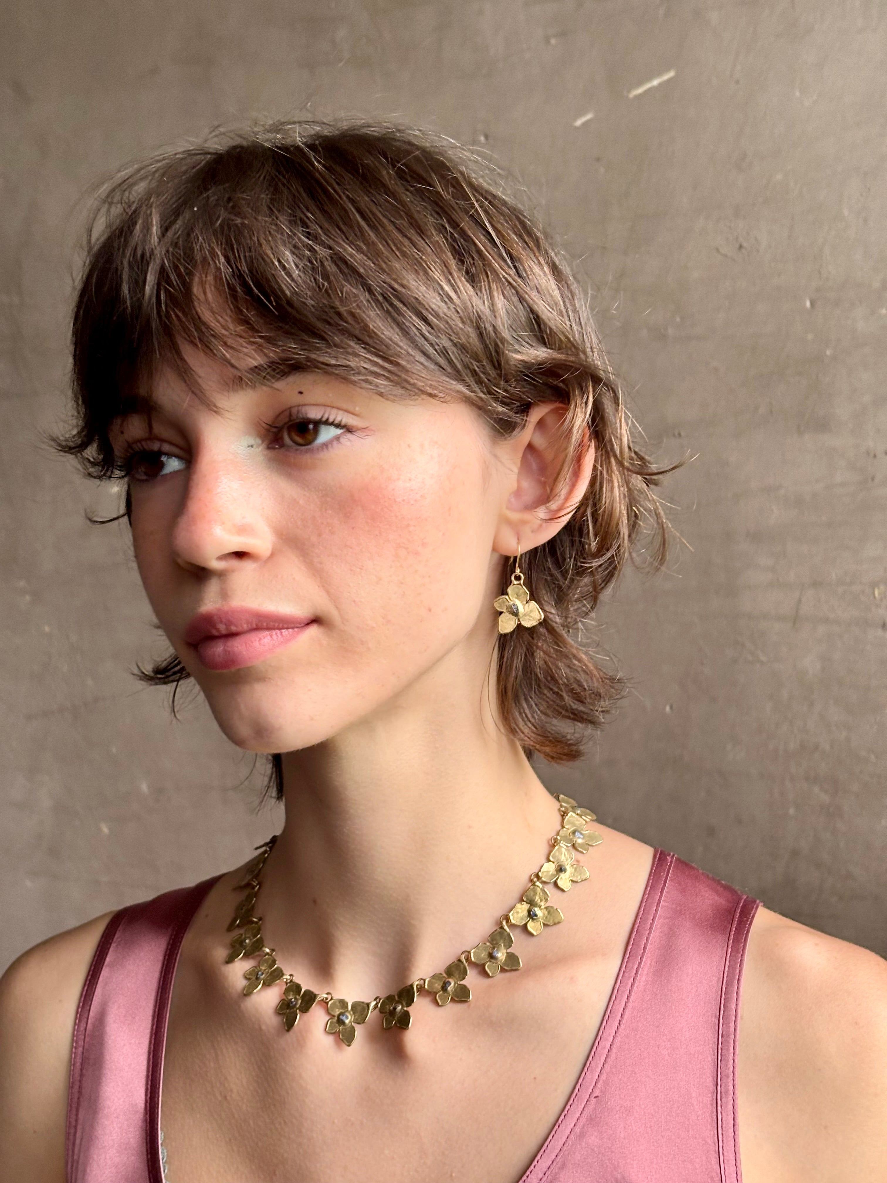 Woman wearing Hydrangea Earrings from New York fine jewelry artist Emilie Shapiro are botanically inspired with Raw sapphires embedded in warm, textured brass dangle from gold wire hoops handcrafted in USA