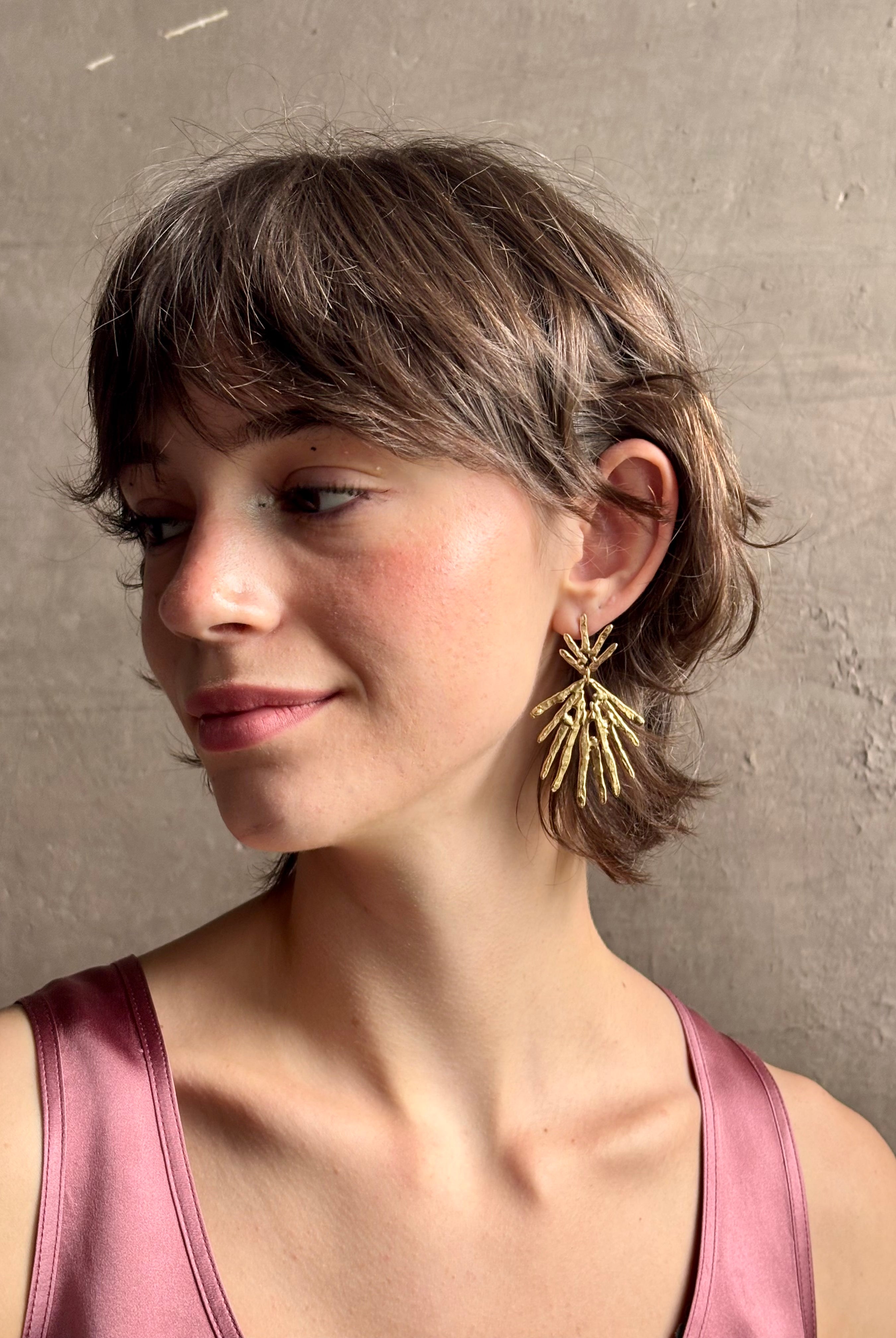 Woman wearing Solaris post Earrings from New York fine jewelry artist Emilie Shapiro that channels the radiant, life-giving energy of the sun in an exquisitely handcrafted textured brass form. Large, statement-making and thoroughly wearable dangle earrings