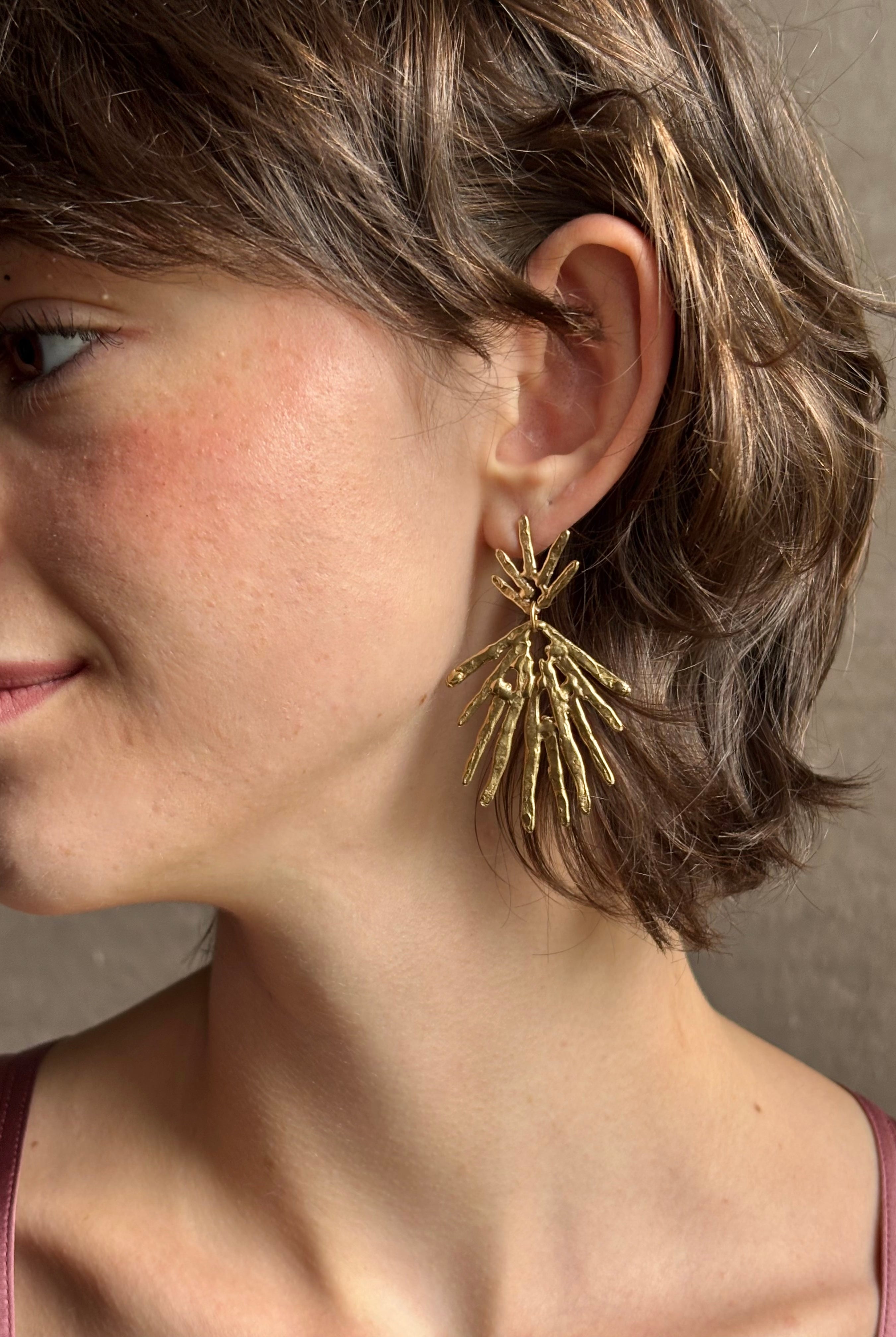 Woman wearing Solaris post Earrings from New York fine jewelry artist Emilie Shapiro that channels the radiant, life-giving energy of the sun in an exquisitely handcrafted textured brass form. Large, statement-making and thoroughly wearable dangle earrings