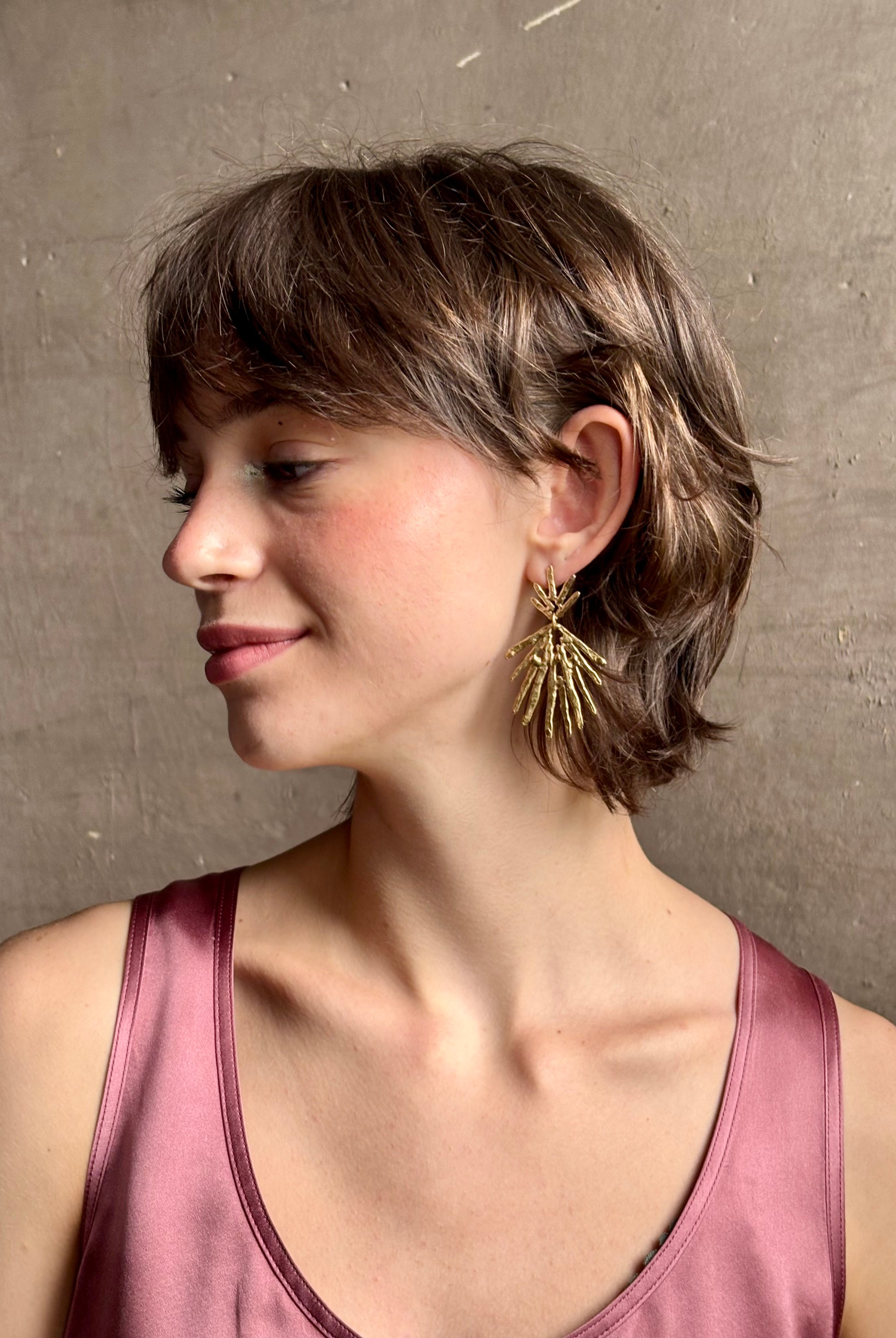 Woman wearing Solaris post Earrings from New York fine jewelry artist Emilie Shapiro that channels the radiant, life-giving energy of the sun in an exquisitely handcrafted textured brass form. Large, statement-making and thoroughly wearable dangle earrings