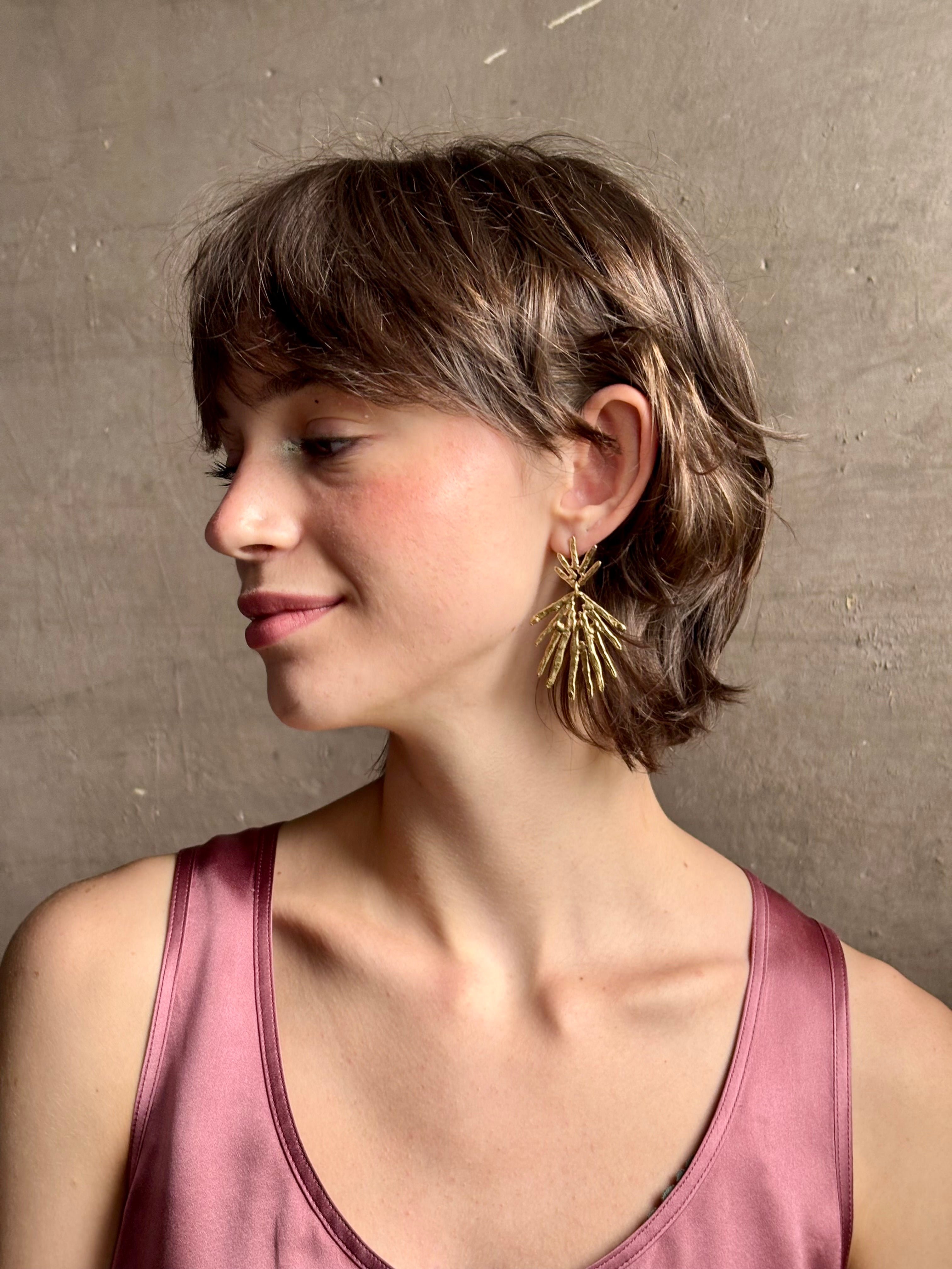 Woman wearing Solaris post Earrings from New York fine jewelry artist Emilie Shapiro that channels the radiant, life-giving energy of the sun in an exquisitely handcrafted textured brass form. Large, statement-making and thoroughly wearable dangle earrings
