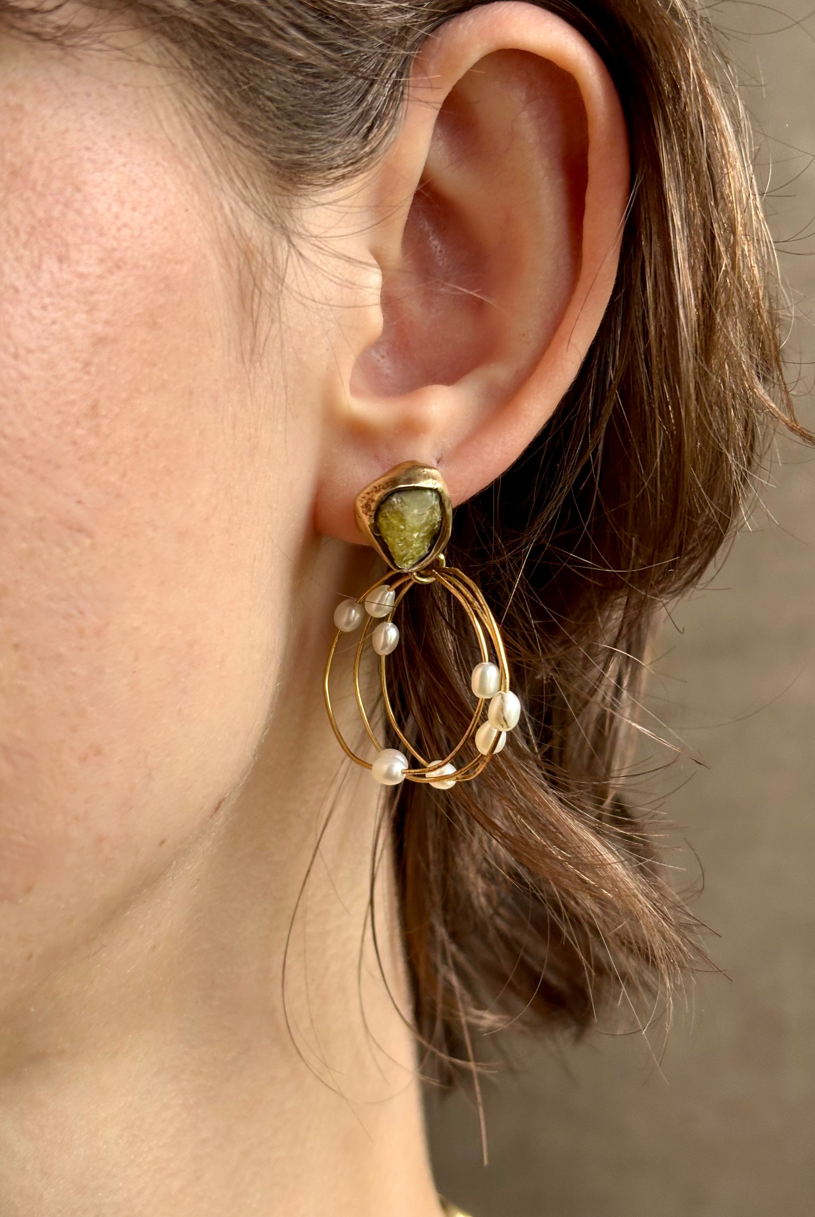 Woman wearing water lily hoop earrings from jewelry designer Emilie Shapiro with posts on Natural garnets individually embedded in warm brass that have three brass circular hoops with three natural white rice pearls on each hoop