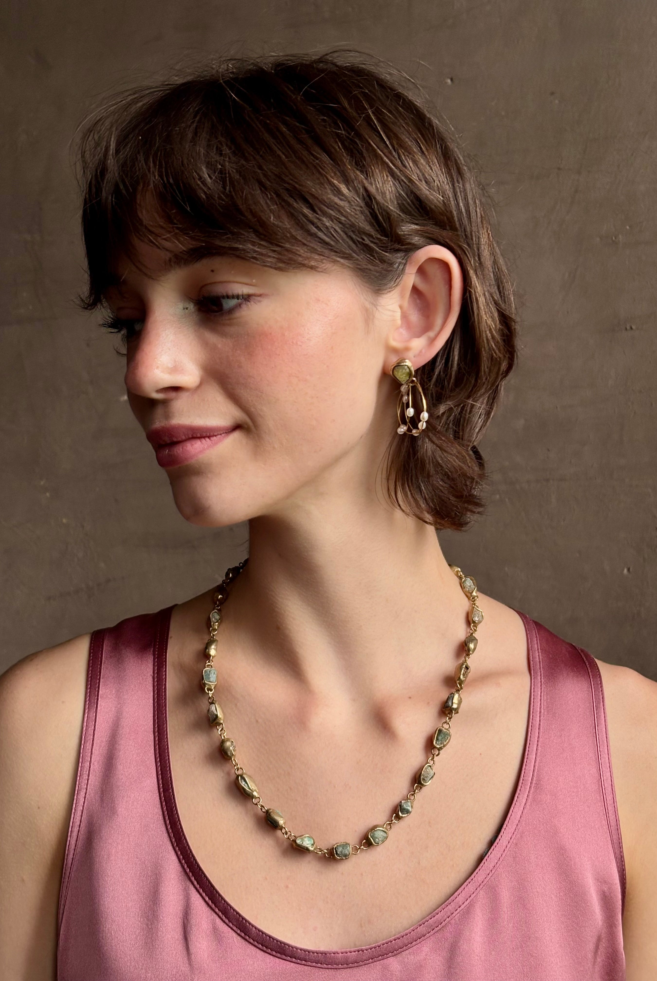 Woman wearing water lily hoop earrings from jewelry designer Emilie Shapiro with posts on Natural garnets individually embedded in warm brass that have three brass circular hoops with three natural white rice pearls on each hoop