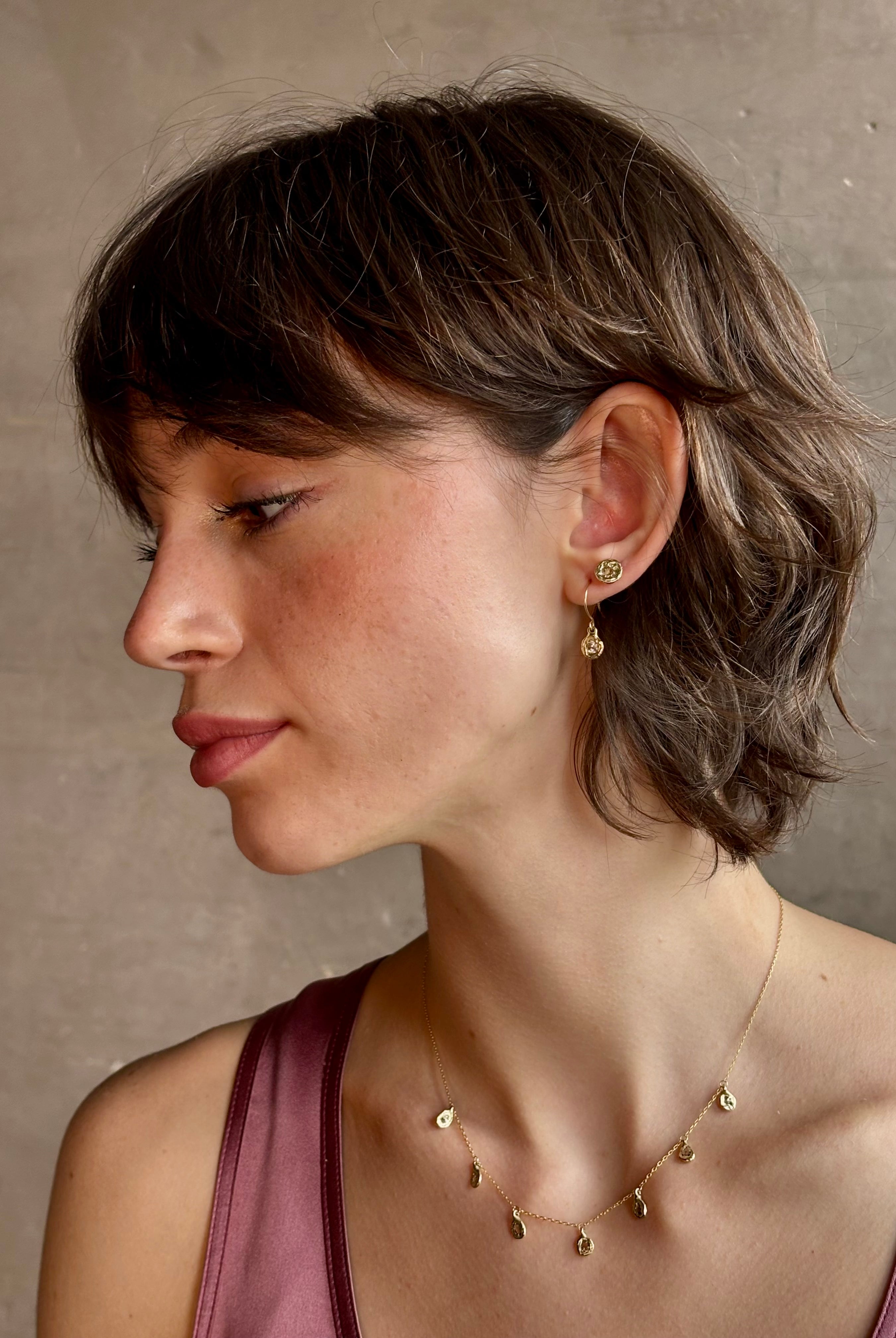 Woman wearing white Sapphire drop earrings from contemporary fine jewelry designer Emilie Shapiro composed of a single round white sapphires set in 14k yellow gold handcrafted in USA