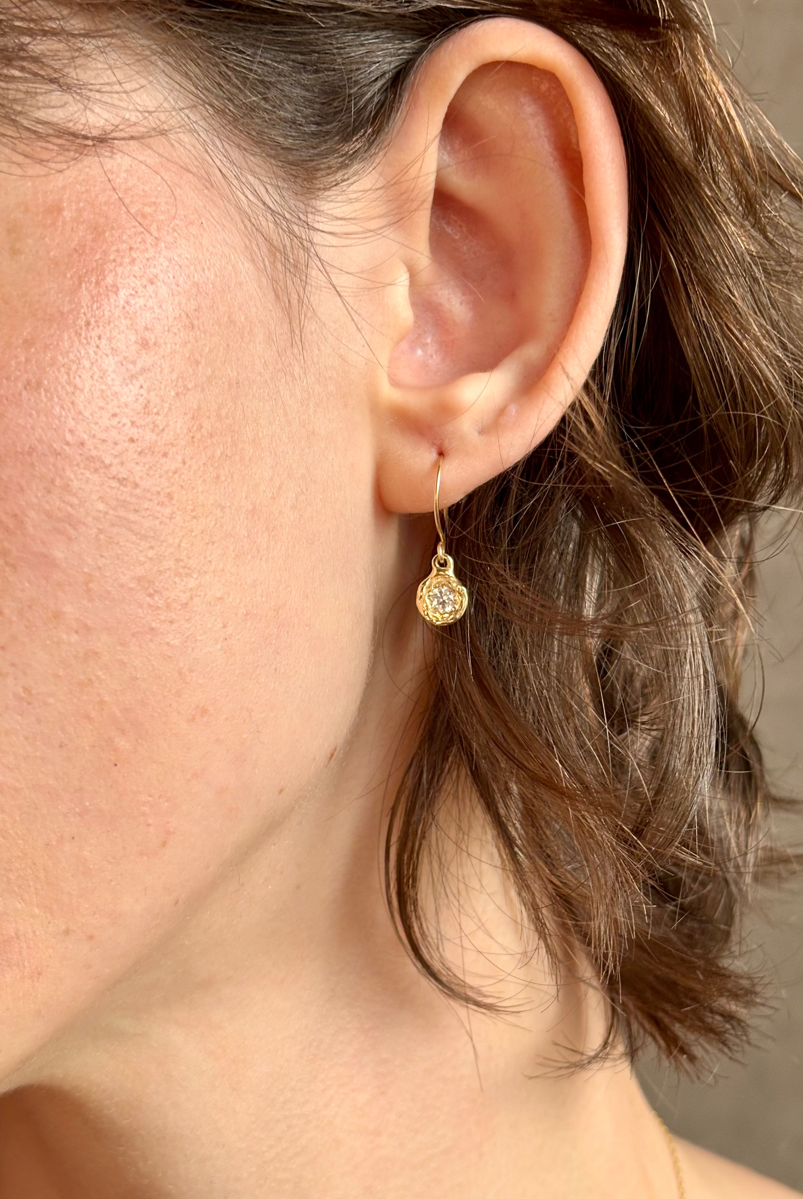 Woman wearing white Sapphire drop earrings from contemporary fine jewelry designer Emilie Shapiro composed of a single round white sapphires set in 14k yellow gold handcrafted in USA