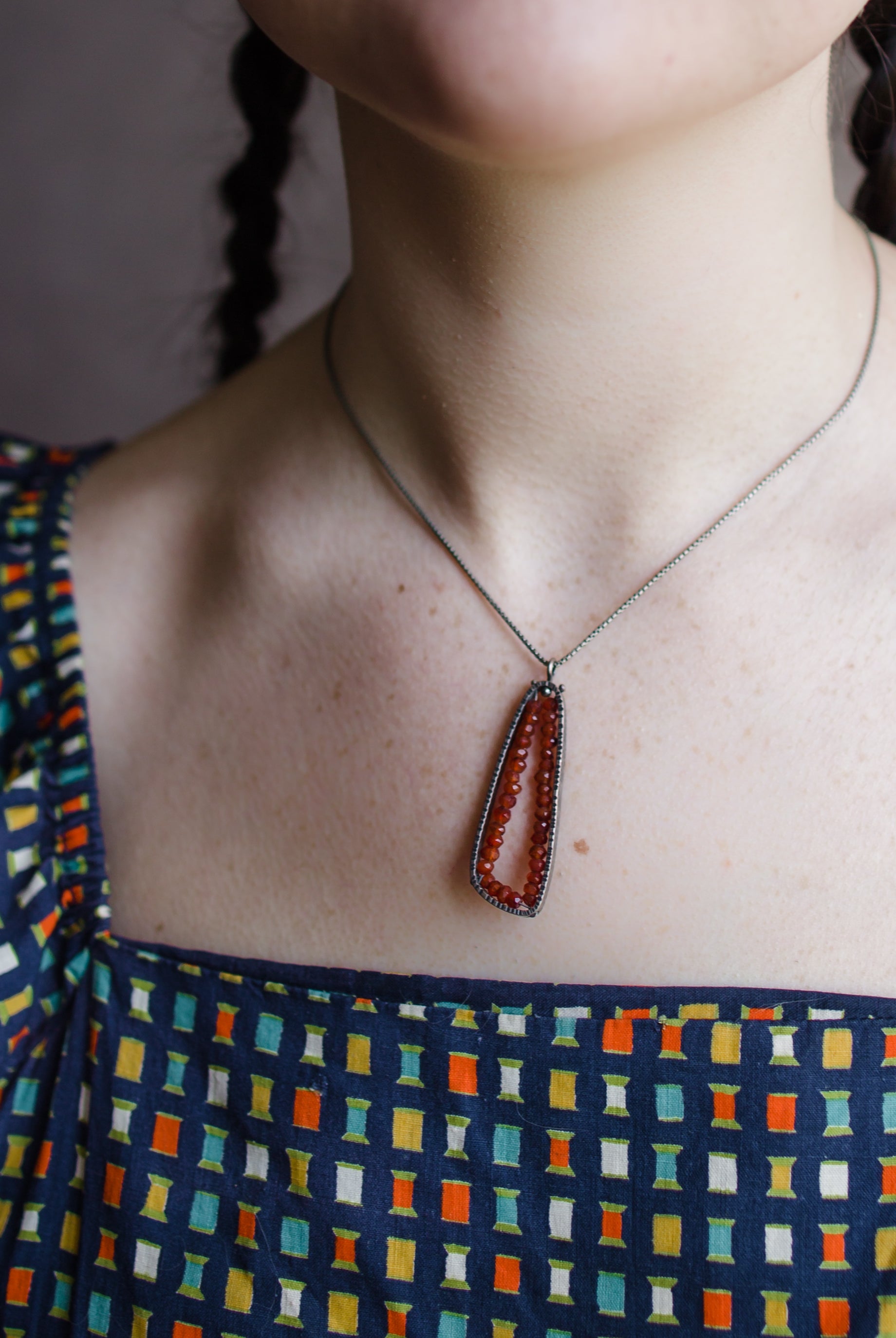 Woman wearing sterling silver trigonal pendant hand hammered texture lined with carnelian stones handmade in USA by fine jewelry artist Erica Bailey