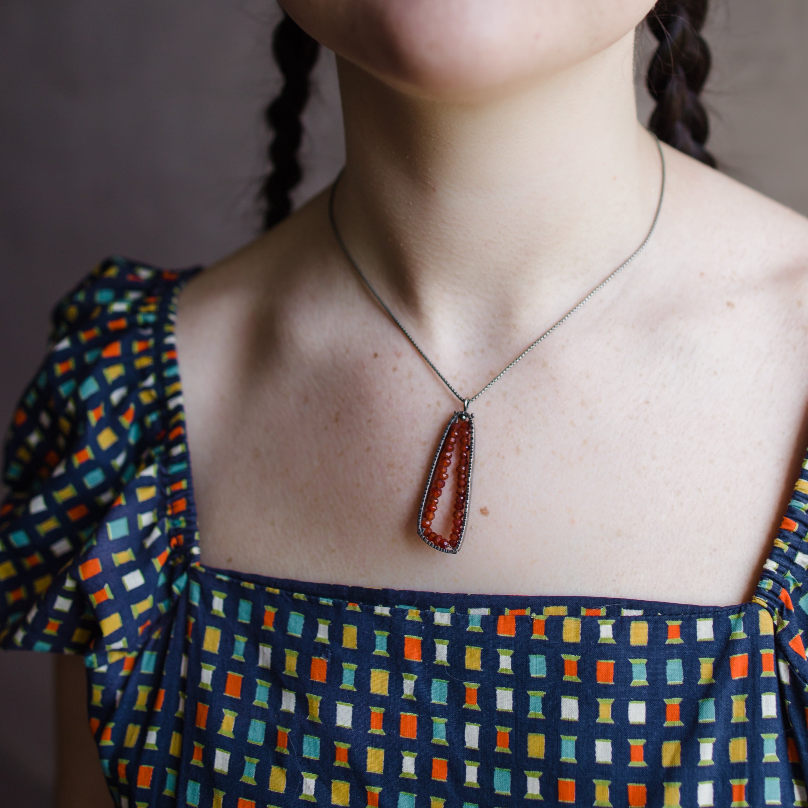 Woman wearing sterling silver trigonal pendant hand hammered texture lined with carnelian stones handmade in USA by fine jewelry artist Erica Bailey