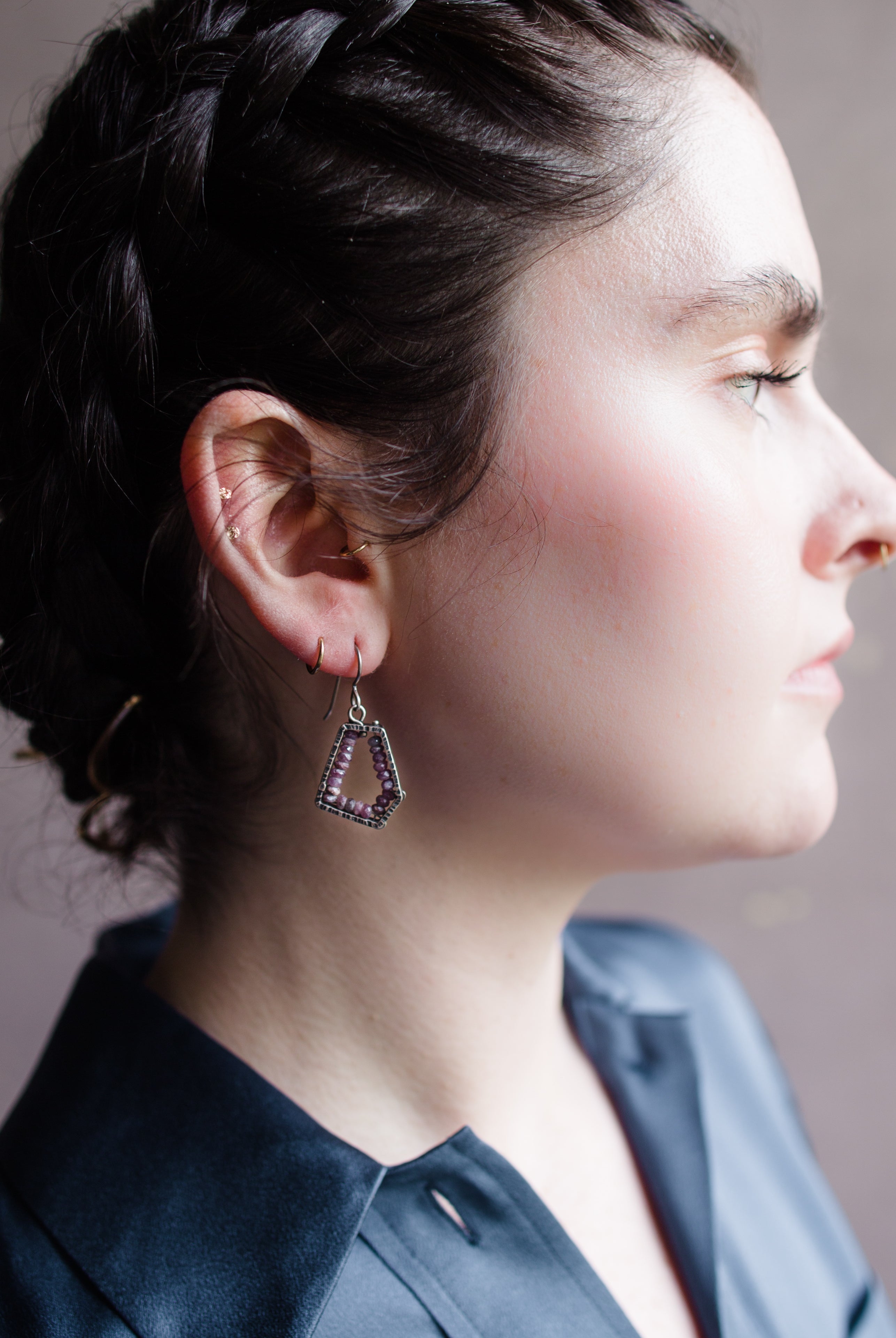 Woman wearing hand hammered sterling silver pentagon frames lined with rubies lining dangling from wire hooks by Erica Bailey