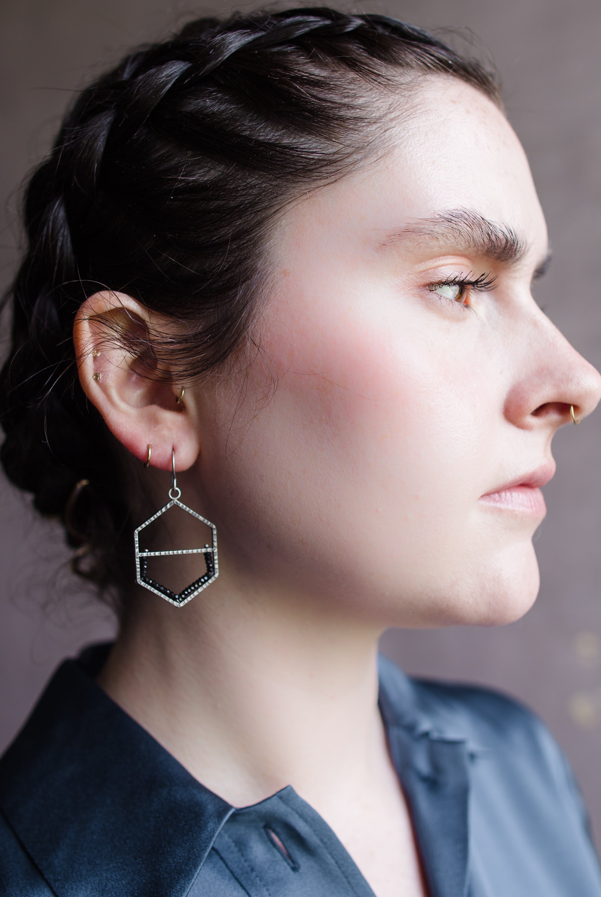 Woman wearing hammered oxidized sterling silver honeycomb shape with bottom of frame is lined in spinel stones on a wire hook