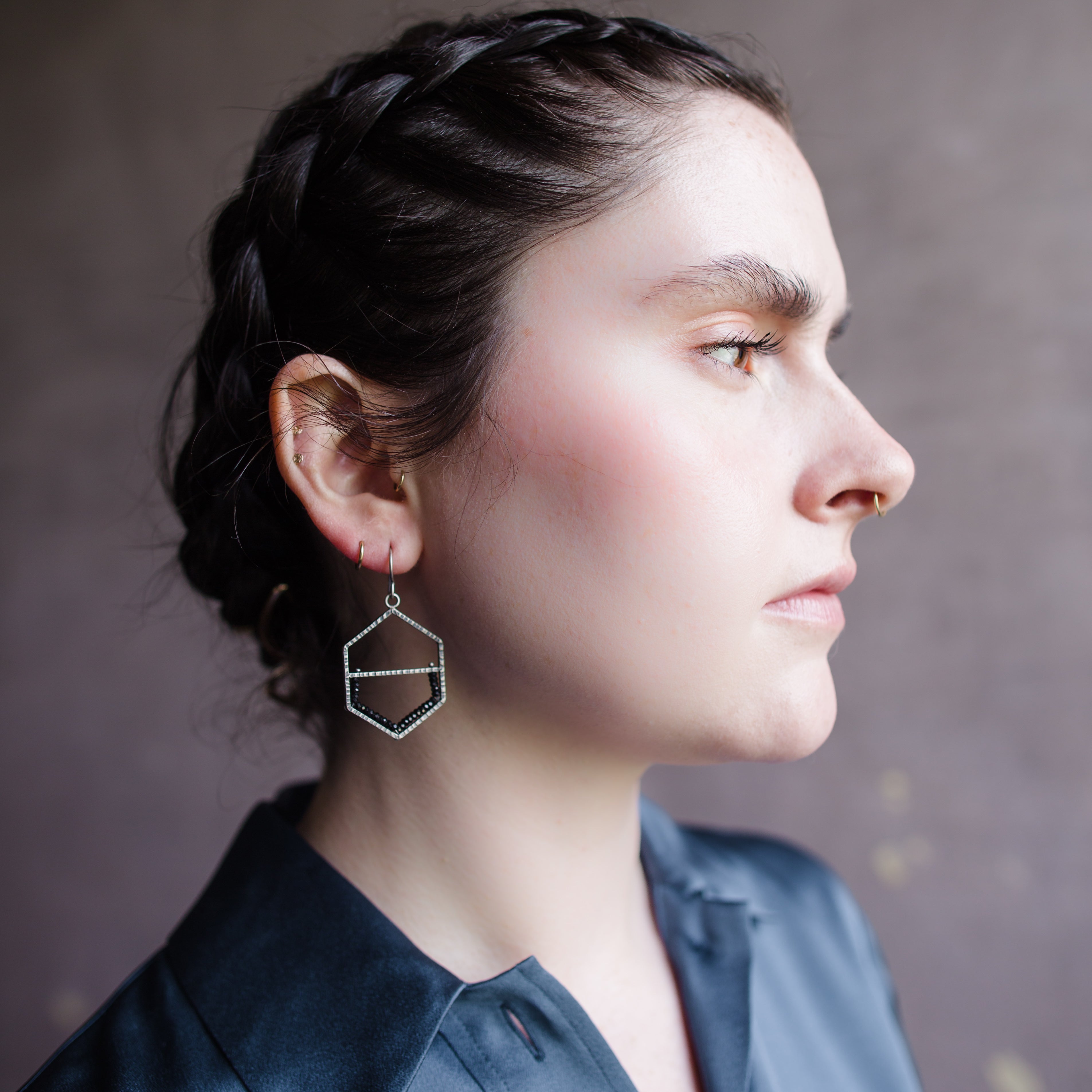 Woman wearing hammered oxidized sterling silver honeycomb shape with bottom of frame is lined in spinel stones on a wire hook
