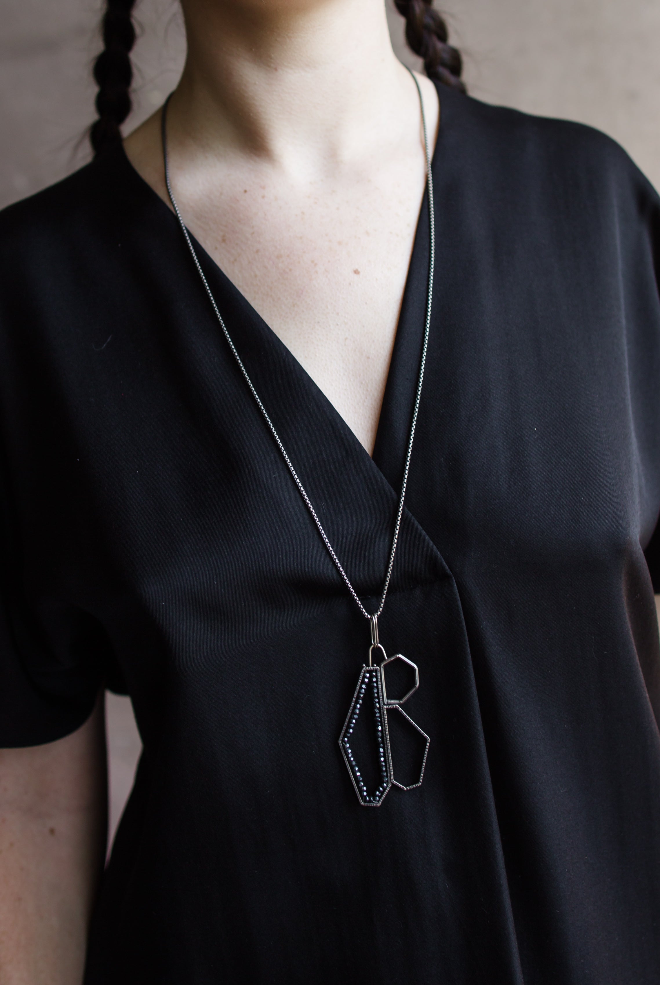 Woman wearing a black top and showcasing a sterling silver and spinel pendant necklace with a geometric design by North Carolina jewelry artist Erica Bailey