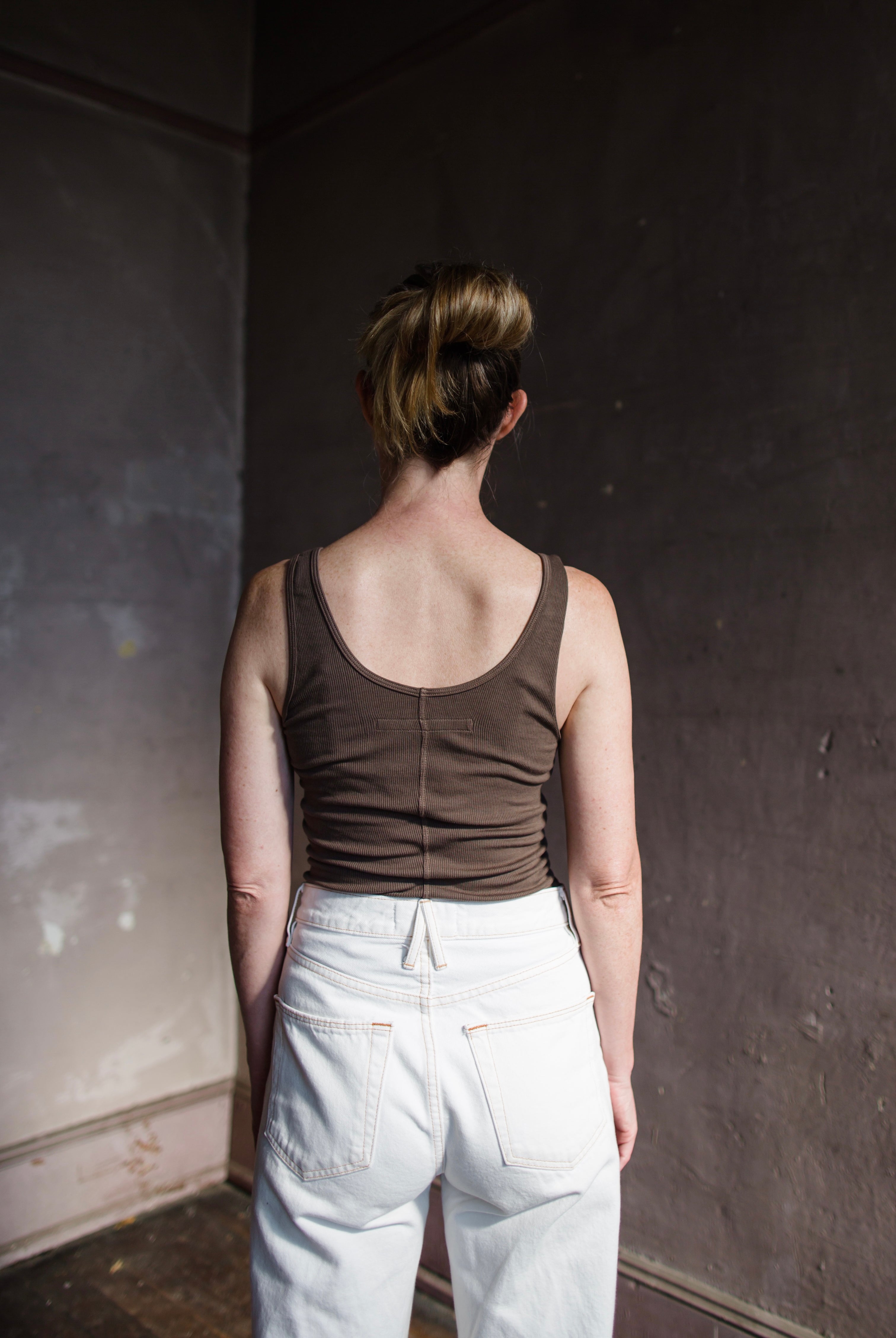 Image featuring a woman wearing the tank top from Enza Costa crafted with soft rib fabric and offers a body-skimming fit with flattering stretch in mushroom brown.