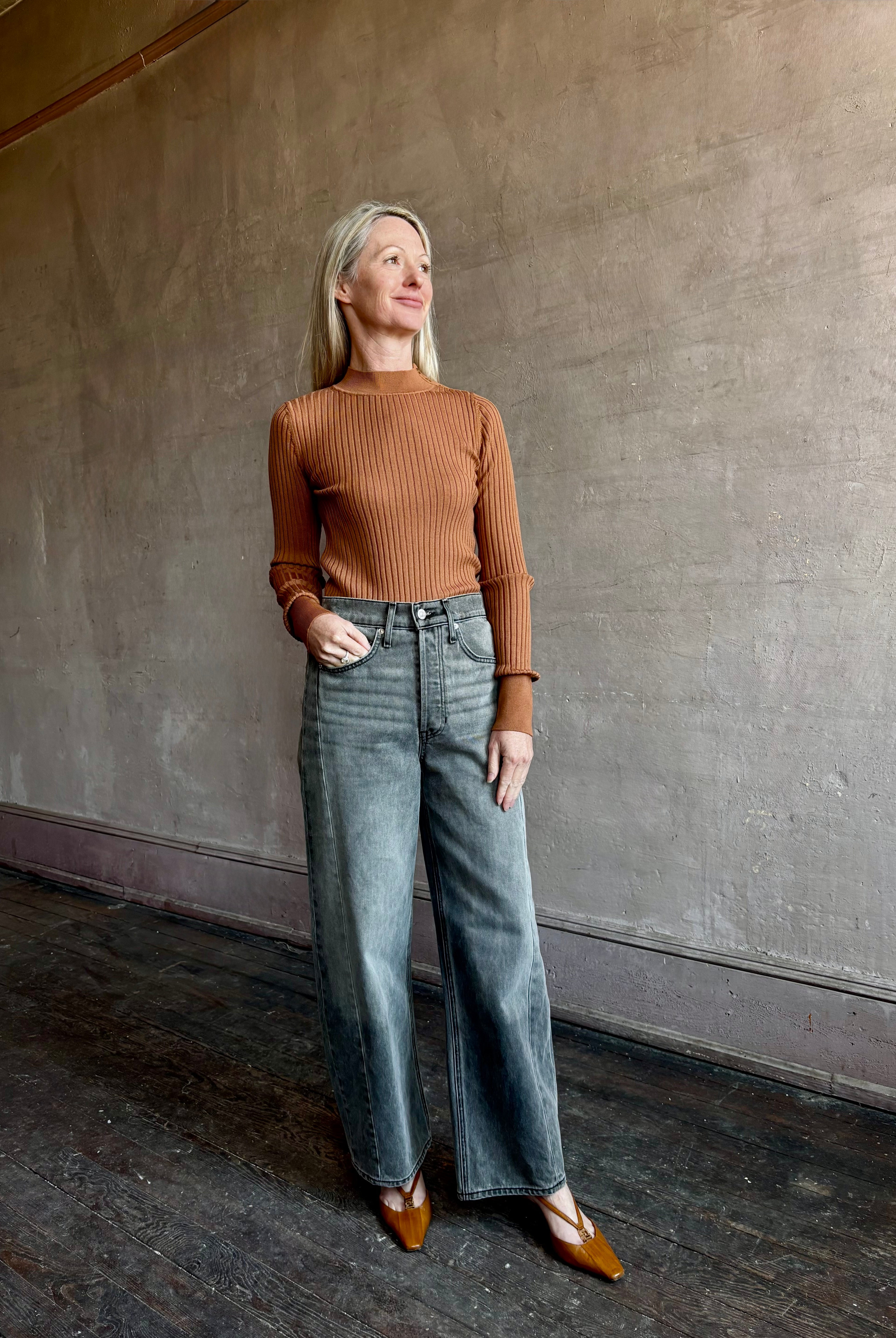 Image of woman wearing luxury Italian Forte Forte Superfine Merino Ribbed Turtleneck Sweater in neutral carmel colorway with long sleeves