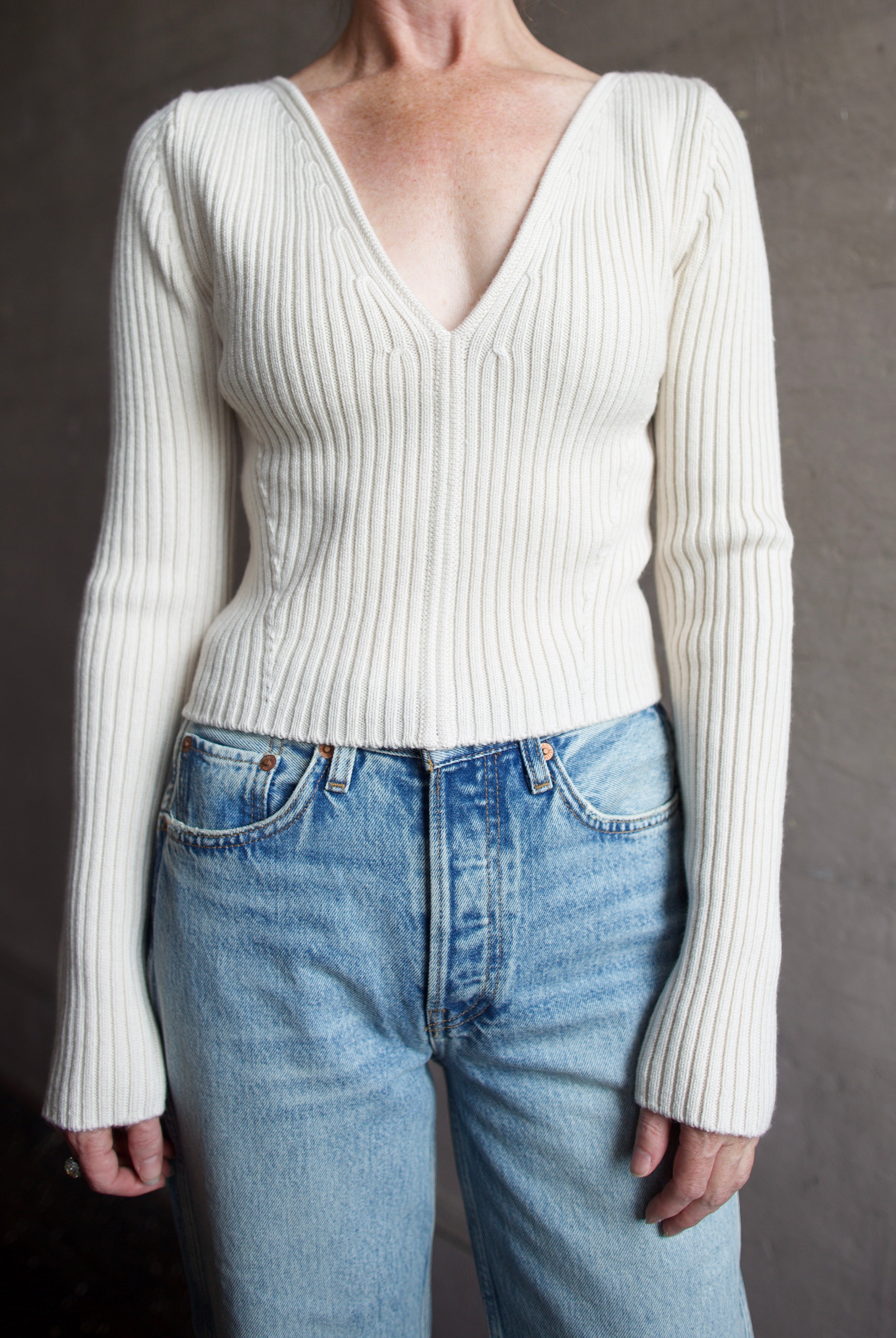 Image featuring a woman wearing the Forte Forte Deep Neckline Ribbed Stretch Merino Sweater with a v-neckline and a cropped fit.