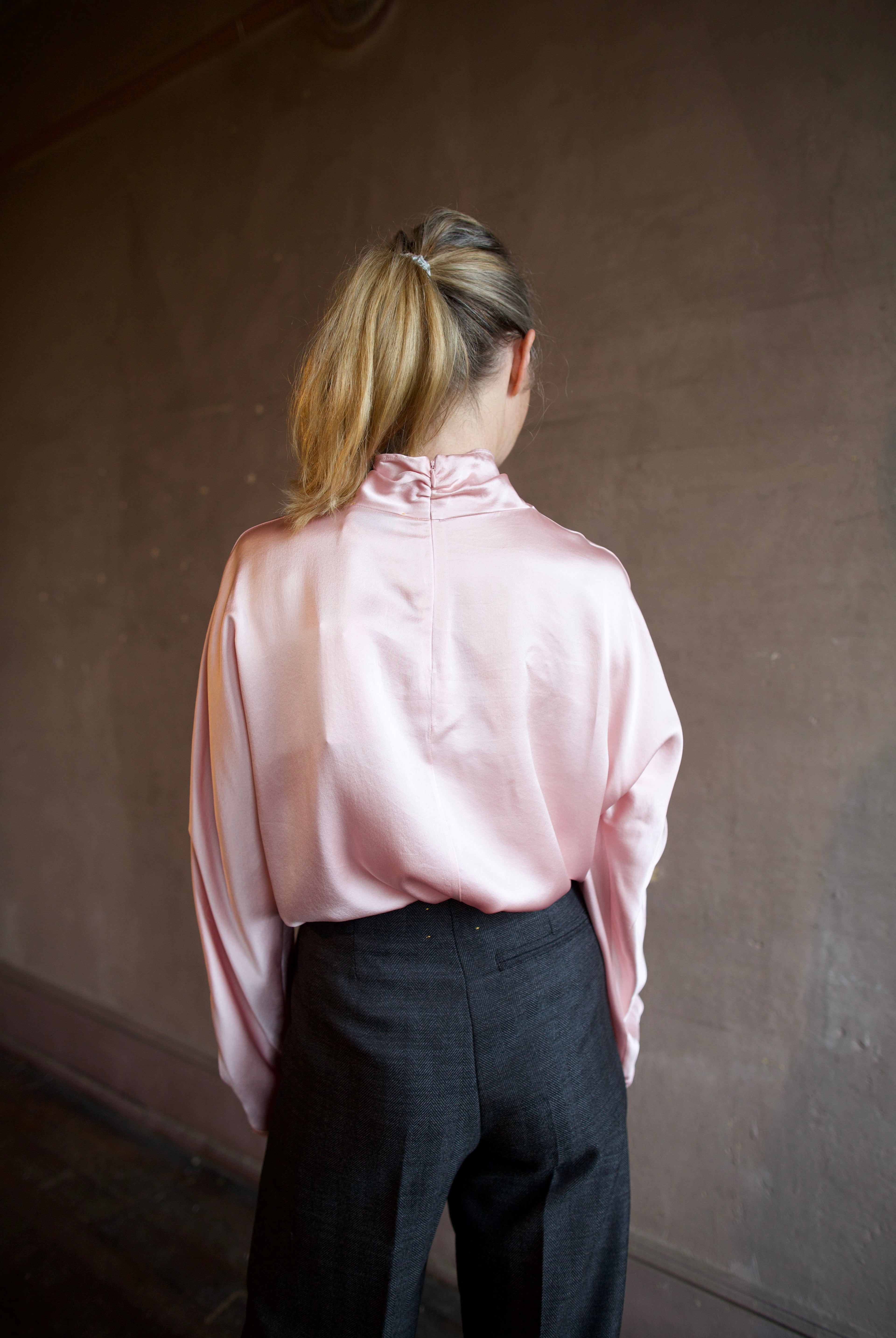 Image featuring a woman wearing the satin crater neck silk shirt by Forte Forte with s a high neckline, zip closure and a relaxed fit in a light pink color.