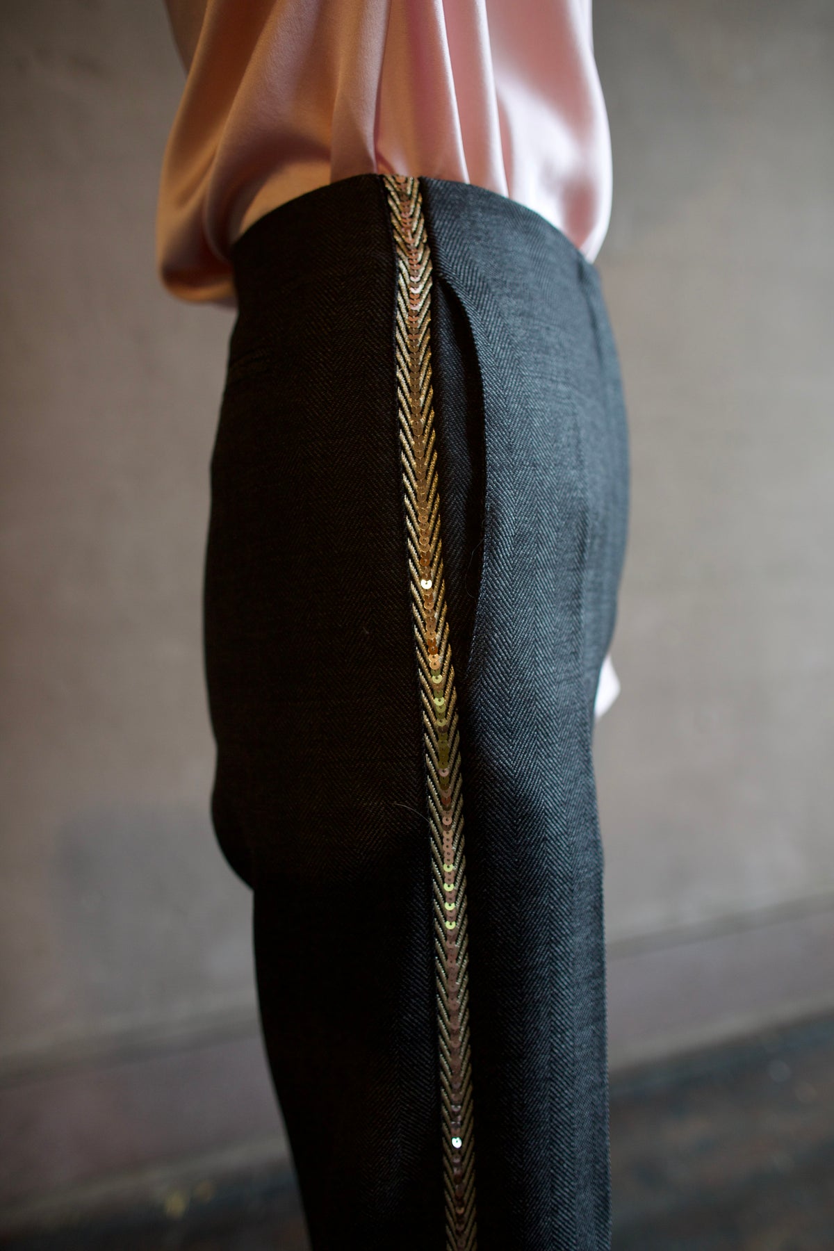 Mature woman wearing Forte_Forte's tailored Grey Herringbone Pants in virgin wool asymmetrical sequence embellishment down side